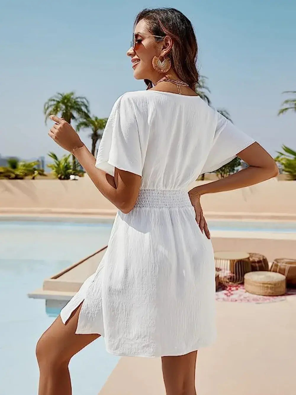 Model wearing a white smocked V-neck short sleeve dress by a pool, showcasing a casual yet elegant style.