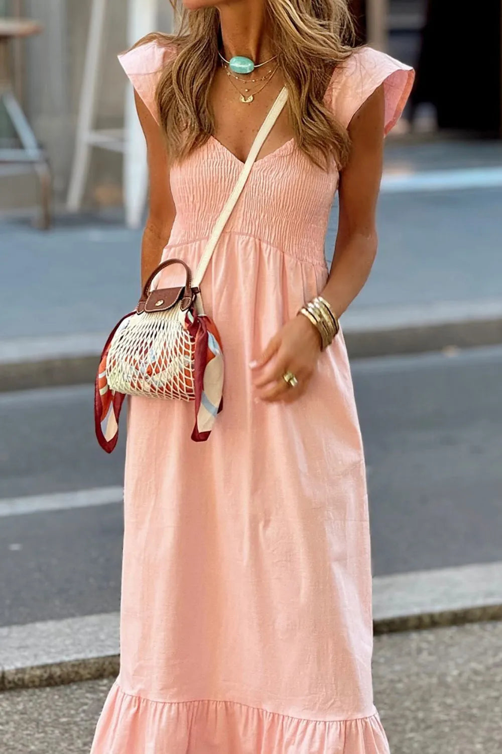 Model wearing a V Neck Ruffled Cap Sleeve Smocked Maxi Dress in soft pink, paired with a stylish handbag and accessories.