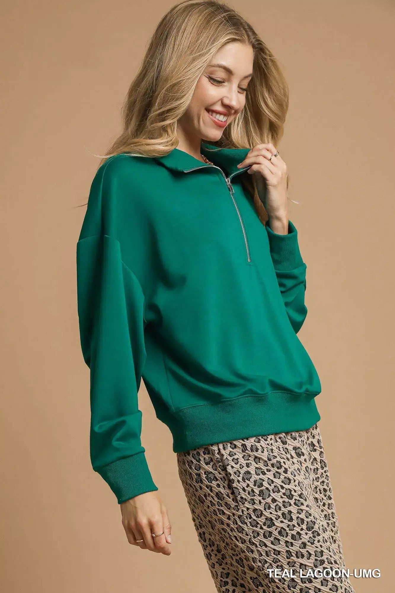 Umgee Half Zip Drop Shoulder Sweatshirt in green worn by a smiling model against a beige background.