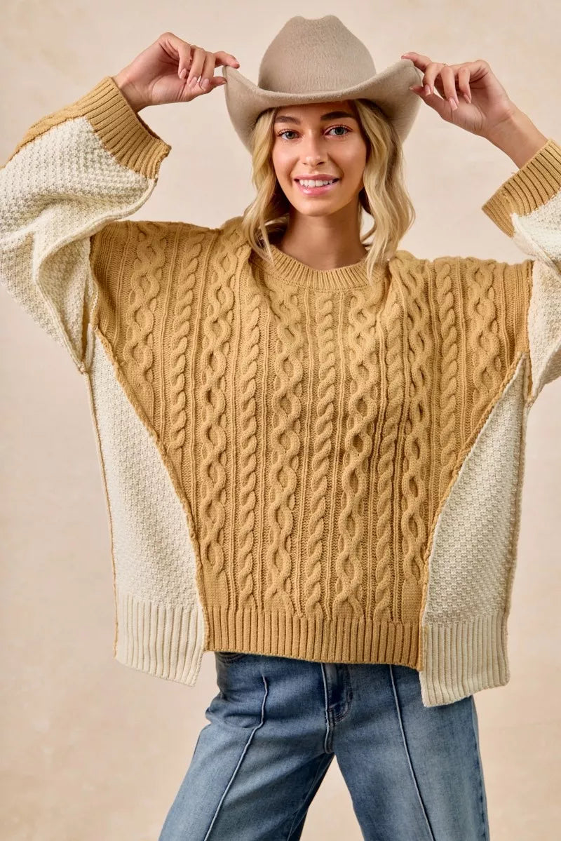 Model wearing BiBi Cable Knit Hacci Combo Sweater with uneven hem, styled with a hat, showcasing its cozy texture.