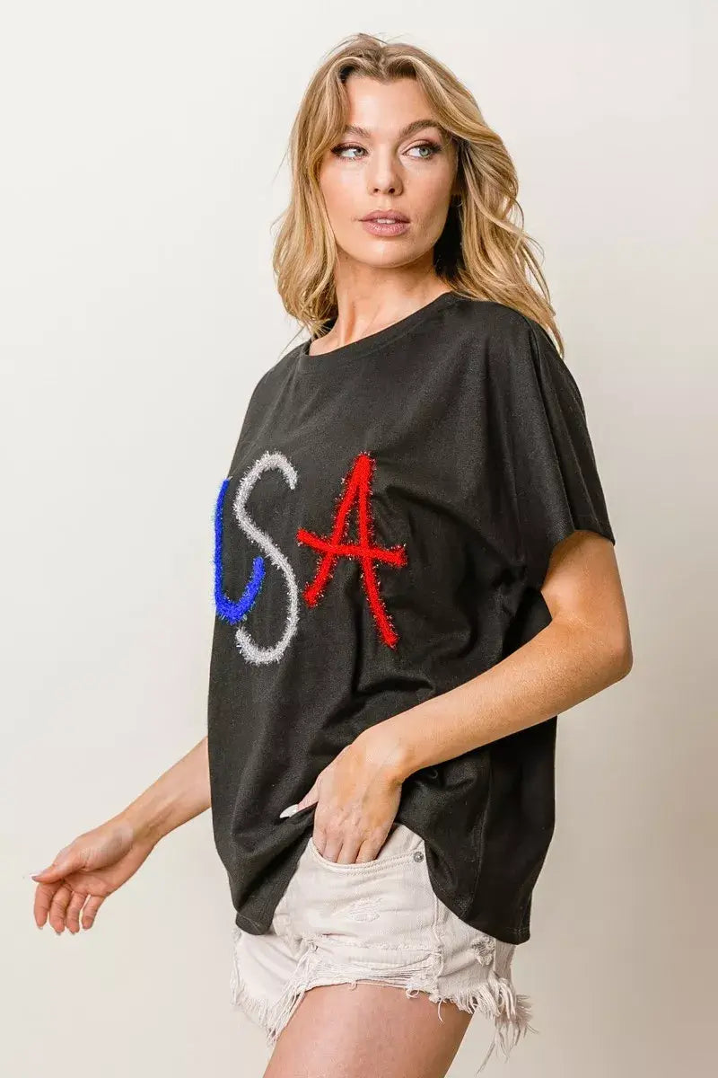 BiBi metallic letter short dolman sleeve top featuring USA lettering in red, white, and blue on a black background.