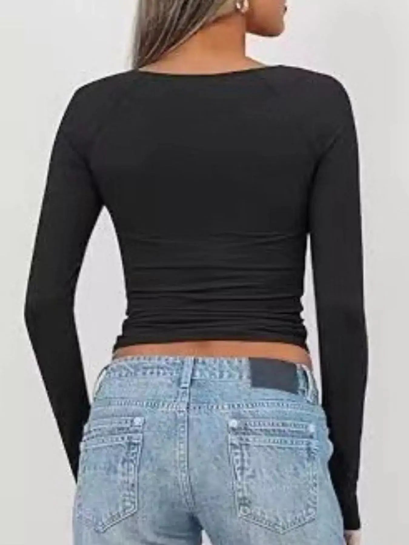 Back view of a woman wearing a black long sleeve fitted t-shirt with a twist front, paired with light blue jeans.