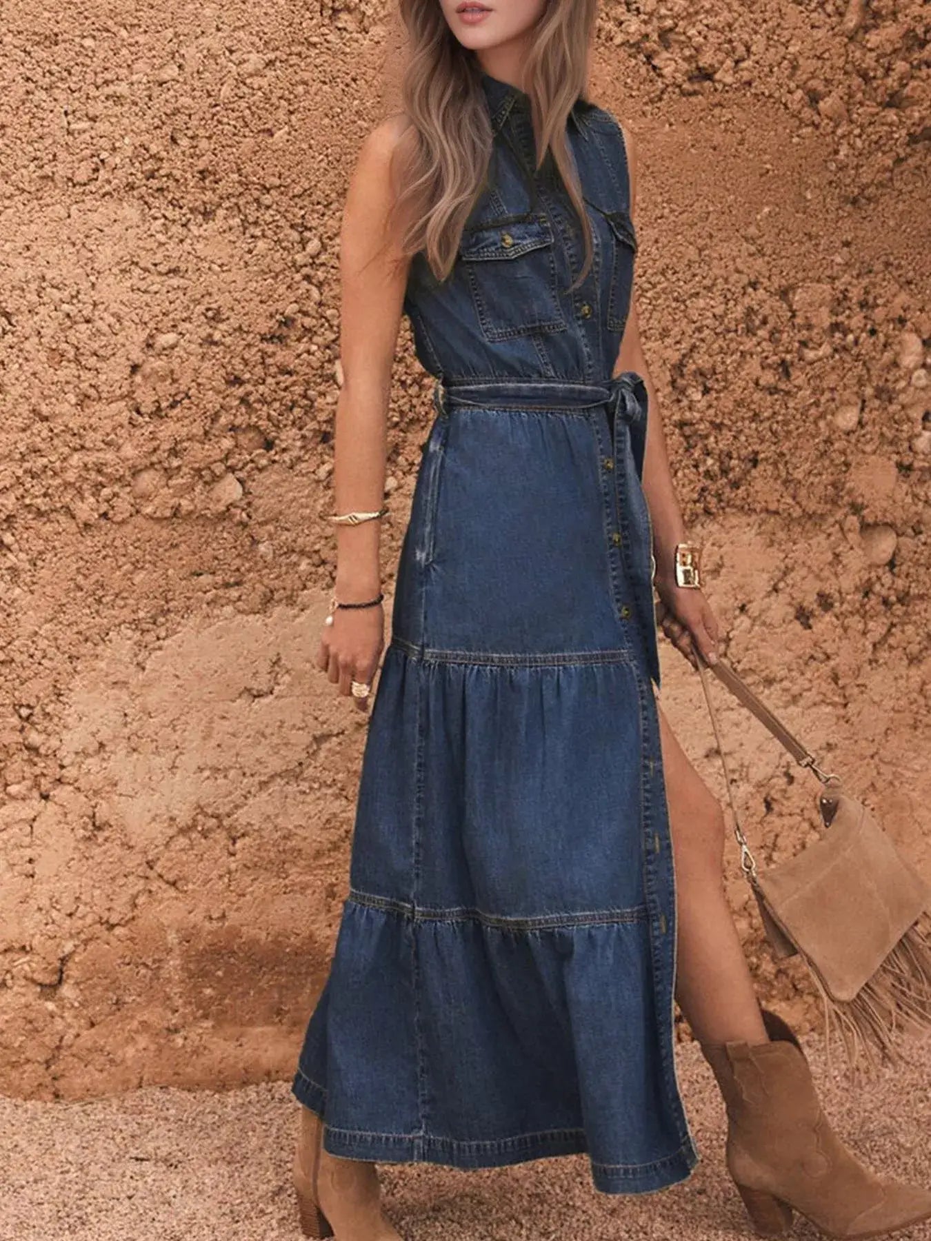 Button front sleeveless denim dress for women styled with a belted waist and casual boots against a textured background.