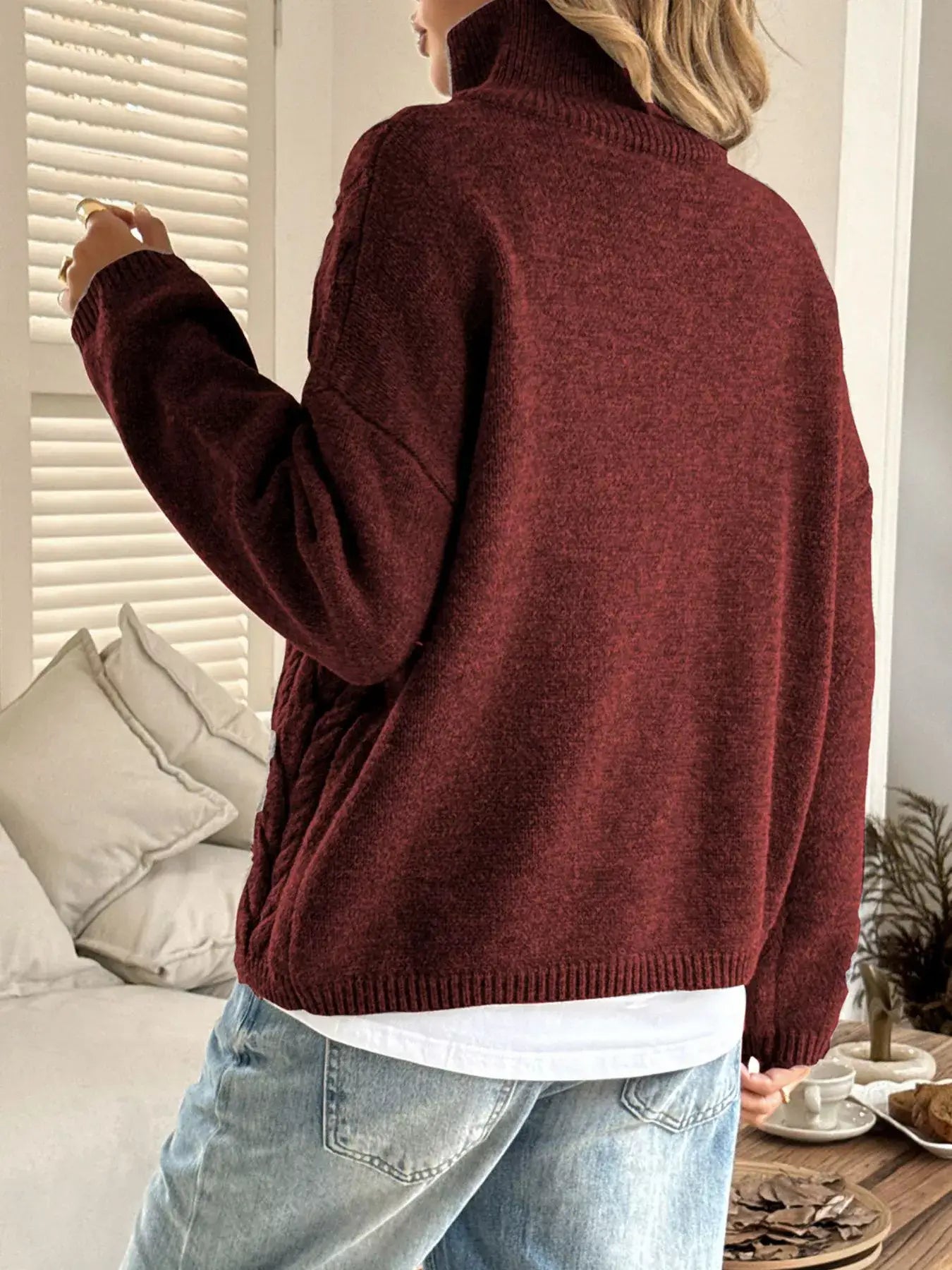 Back view of a woman wearing a zip collar cable-knit sweater in burgundy, showcasing its chunky knit and cozy design.