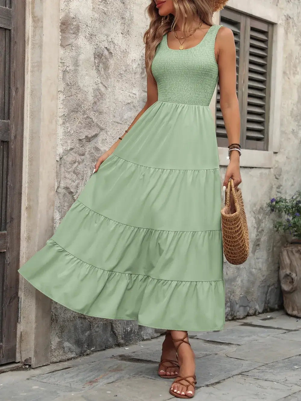 Woman in a light green smocked scoop neck sleeveless tank dress with tiered ruffles, standing outdoors.