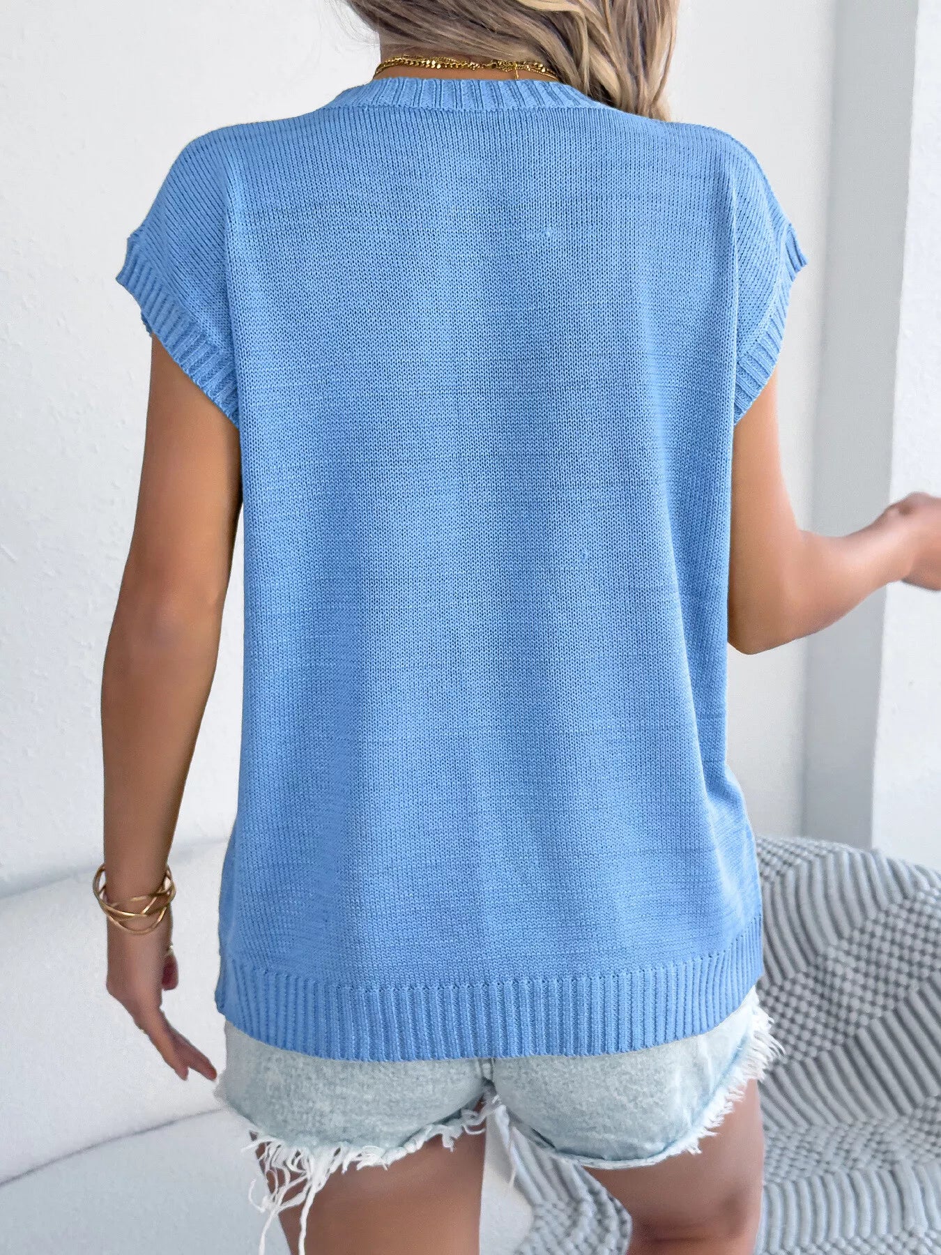 Back view of a woman wearing a light blue Flower Round Neck Sweater with a relaxed fit, paired with denim shorts.