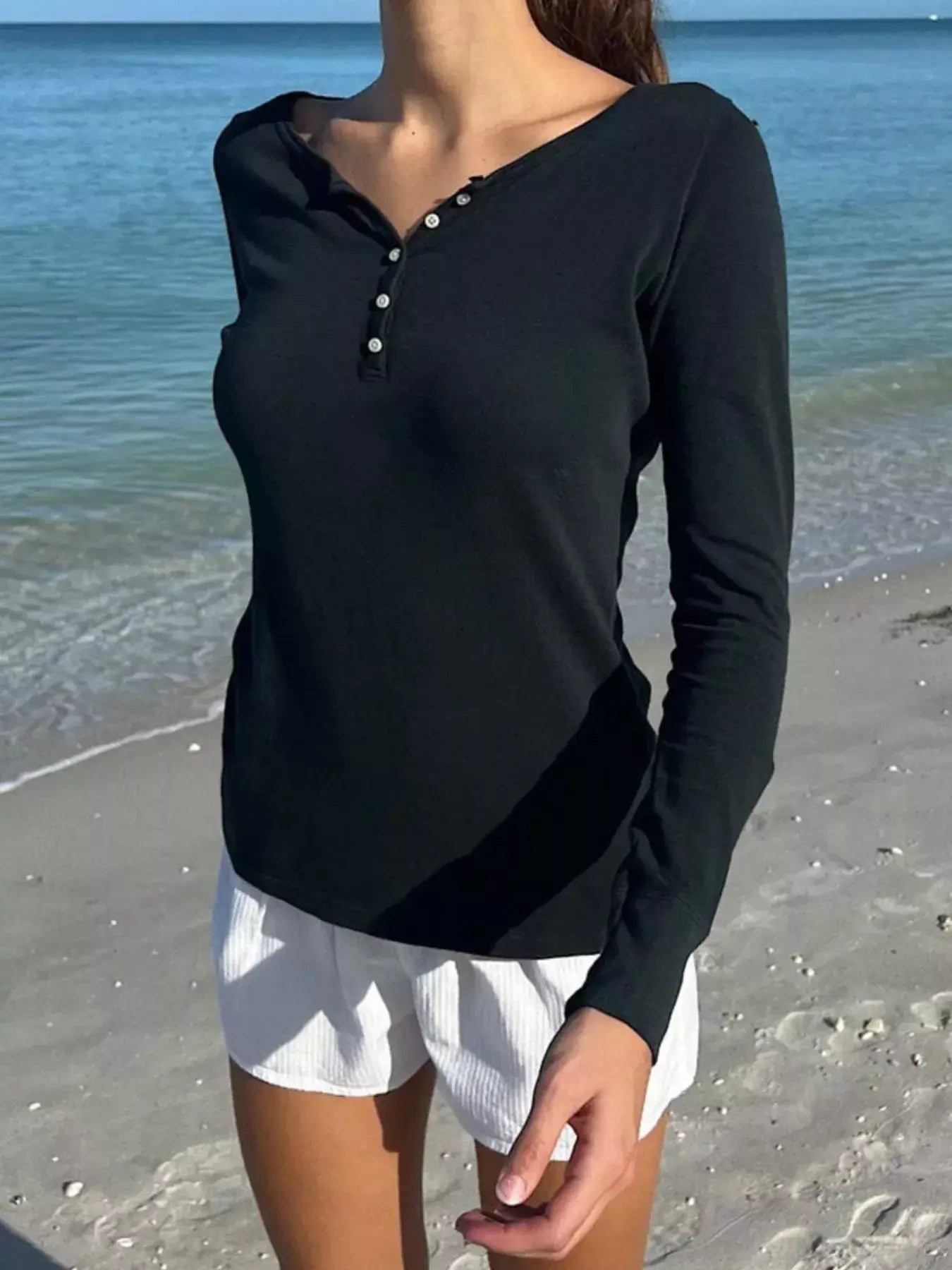 Model wearing a black striped long sleeve Henley t-shirt by the beach, showcasing a casual and stylish look.