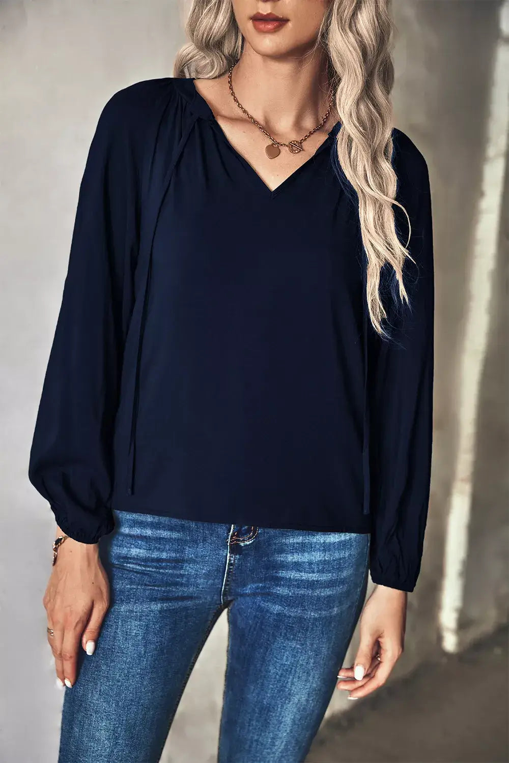 Model wearing a tie neck long sleeve blouse in navy blue, paired with blue jeans for a chic office look.