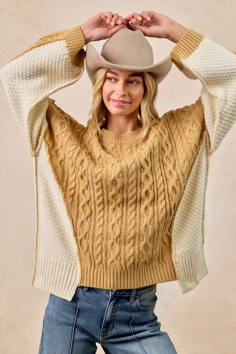 Woman wearing BiBi Cable Knit Hacci Combo Sweater with uneven hem and a cowboy hat, showcasing a stylish look.