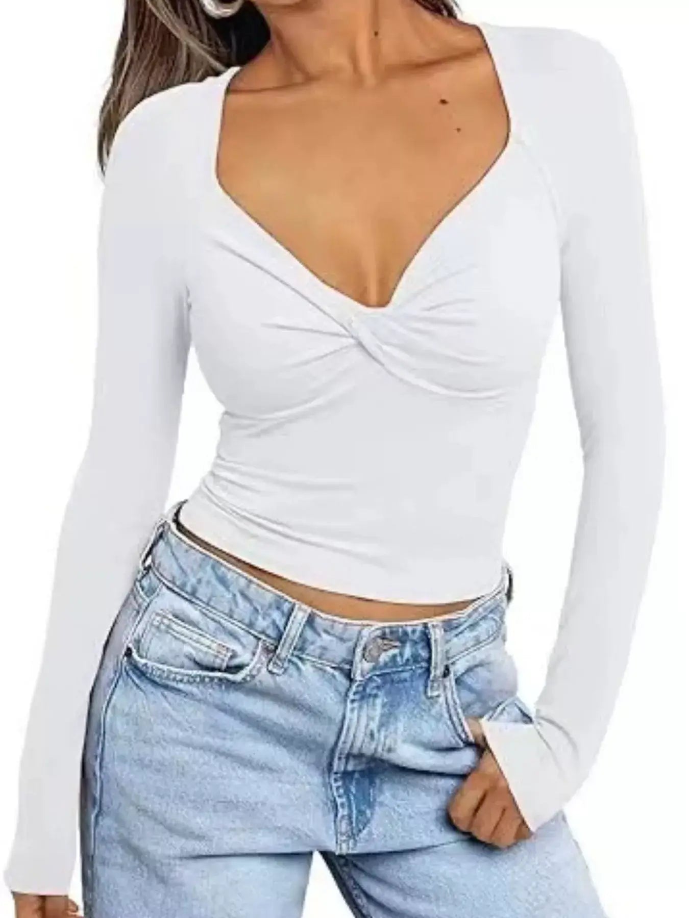 Woman wearing a white twist front long sleeve fitted t-shirt paired with denim jeans, showcasing a chic and stylish look.