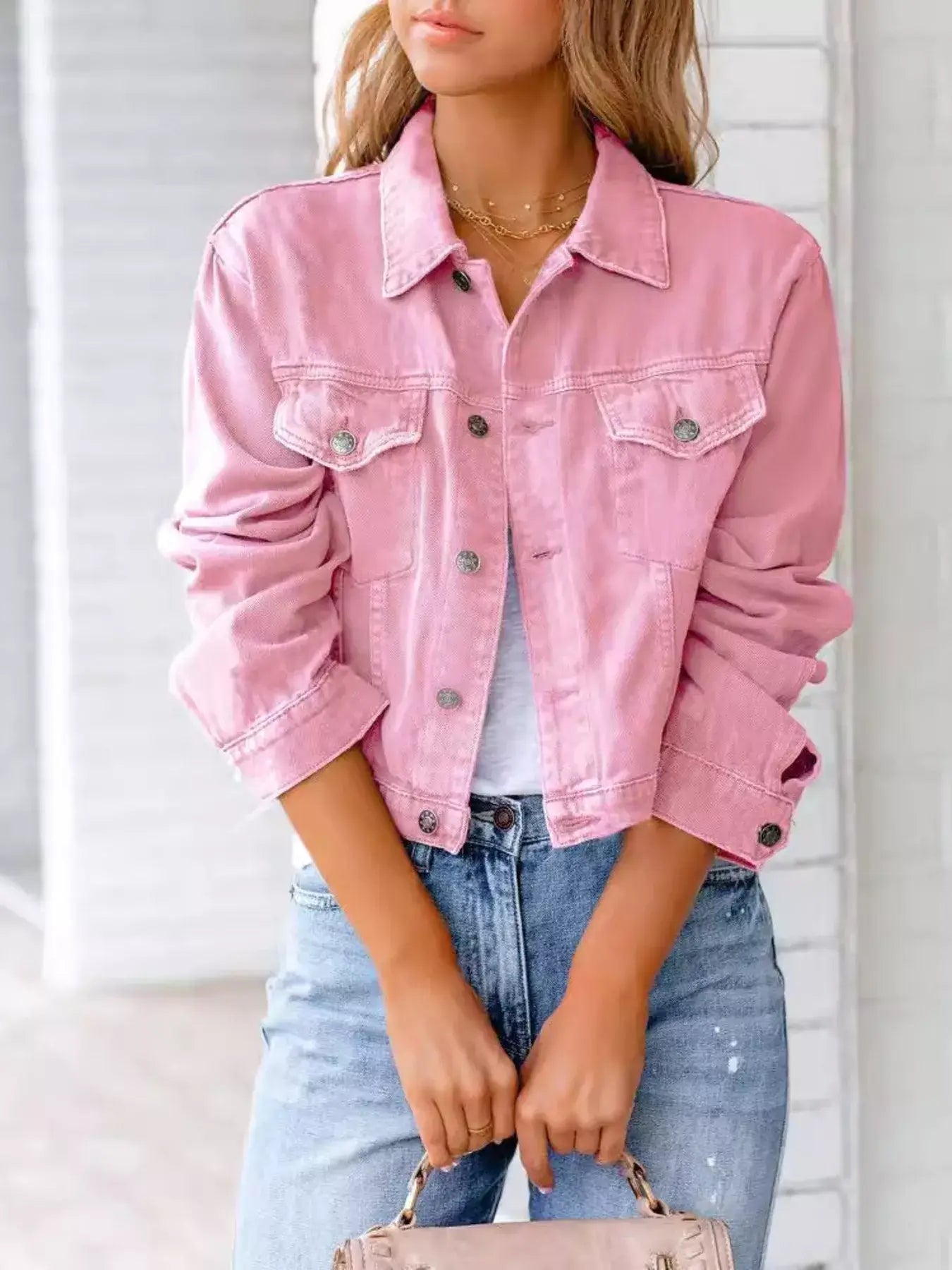 Woman wearing a pink button-up denim jacket with long sleeves and a casual outfit.