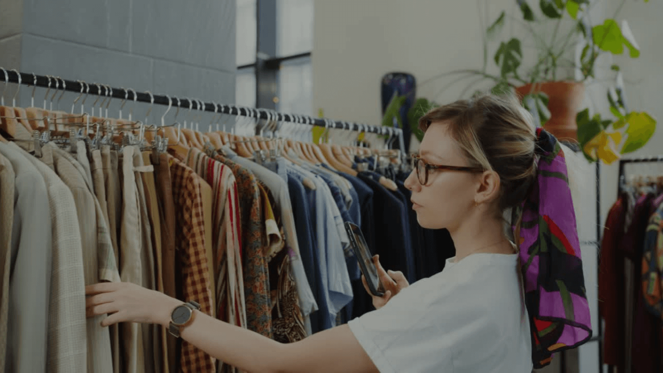Young woman shopping for clothes in a boutique, browsing suits and dresses on display racks.