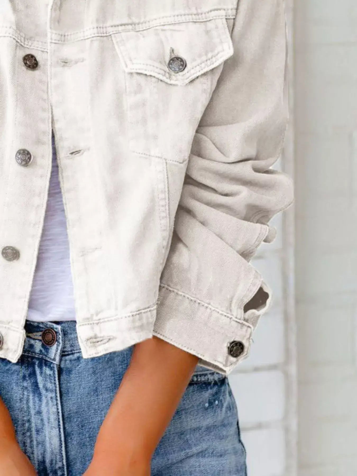 Close-up of a woman wearing a beige button-up long sleeve denim jacket with rolled sleeves.