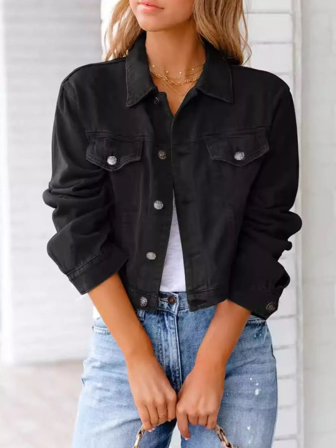 Woman wearing a black button-up long sleeve denim jacket over a white top with blue jeans.