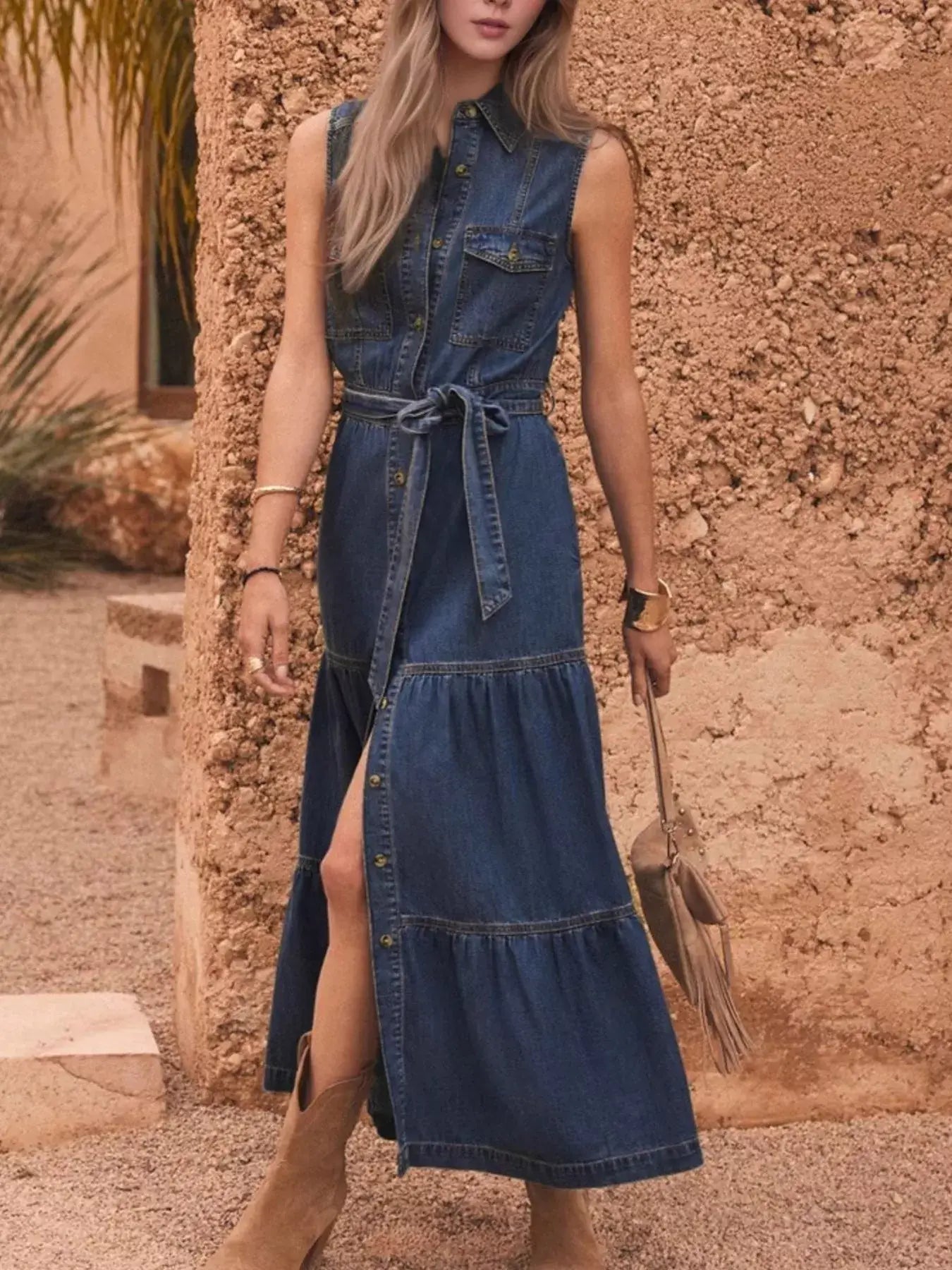Model wearing a button front sleeveless denim dress with a belted waist, showcasing a chic A-line cut and stylish look.