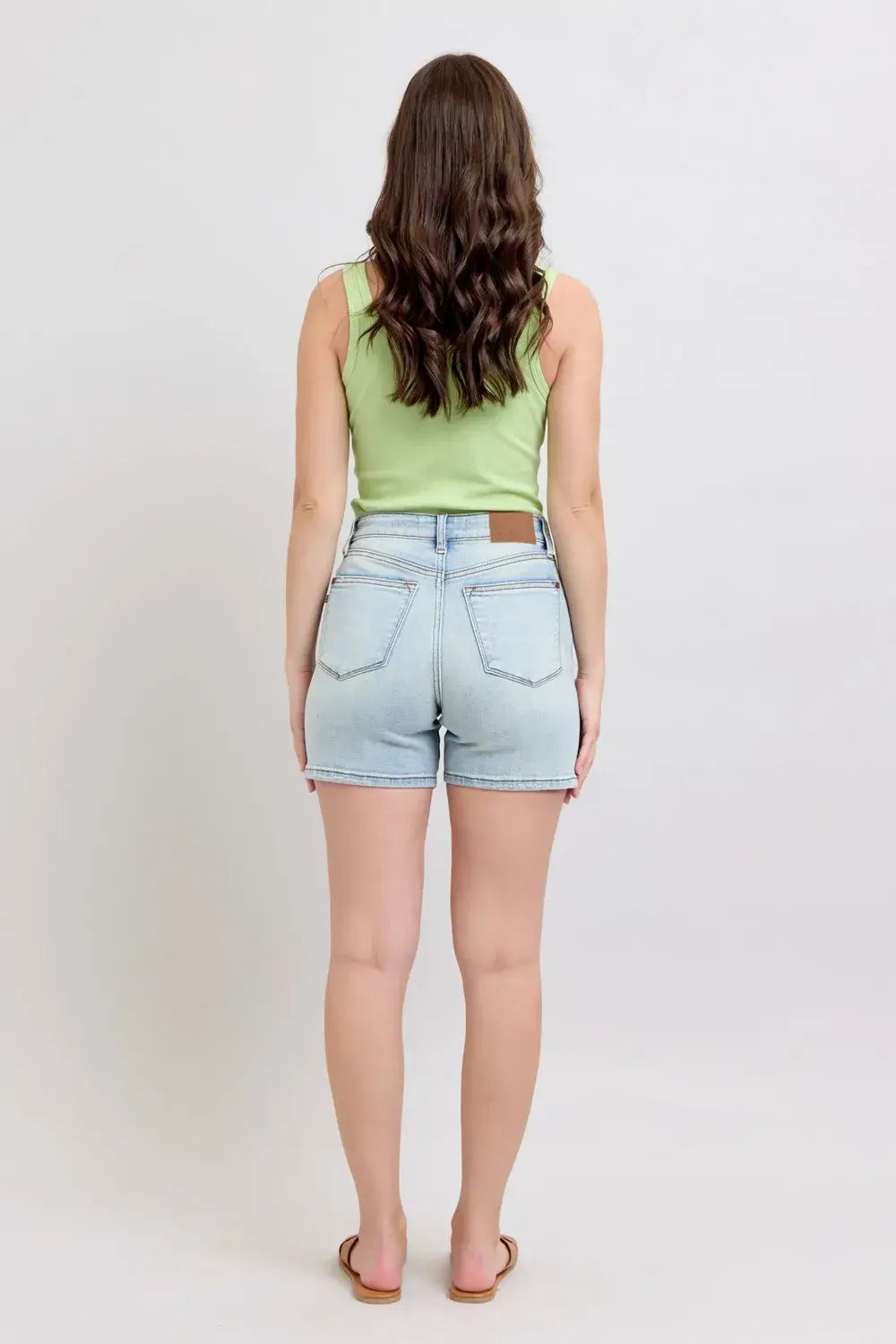 Back view of a model wearing Judy Blue Plus Size Denim Shorts with a green tank top and sandals.