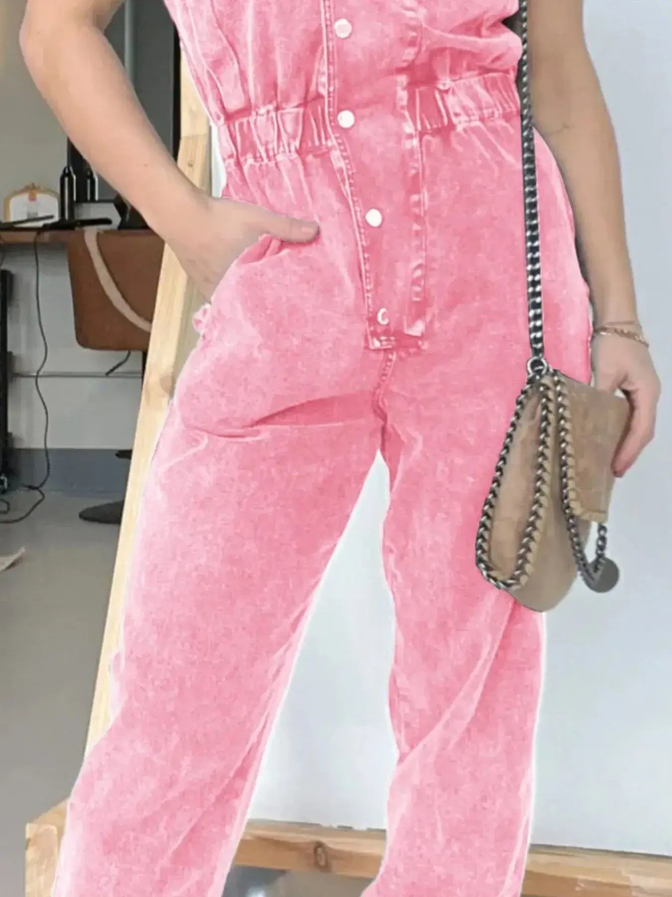 Model wearing a pink button front denim jumpsuit with cap sleeves and a stylish handbag.