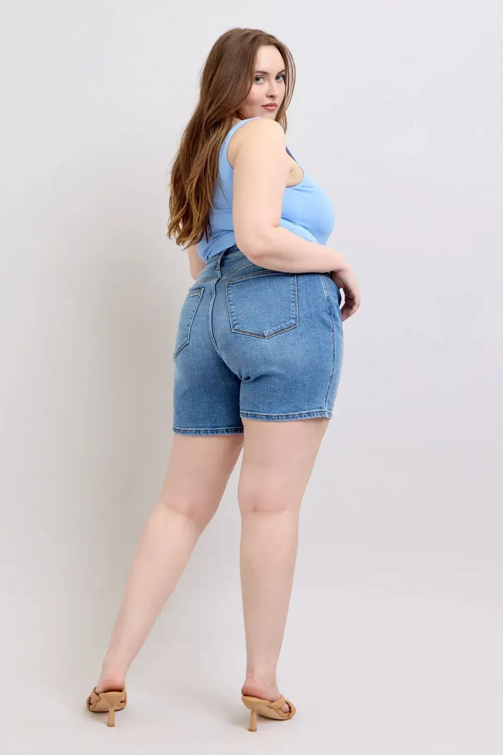 Model wearing Judy Blue Plus Size Denim Shorts with 2-button design and pockets, showcasing a flattering back view.