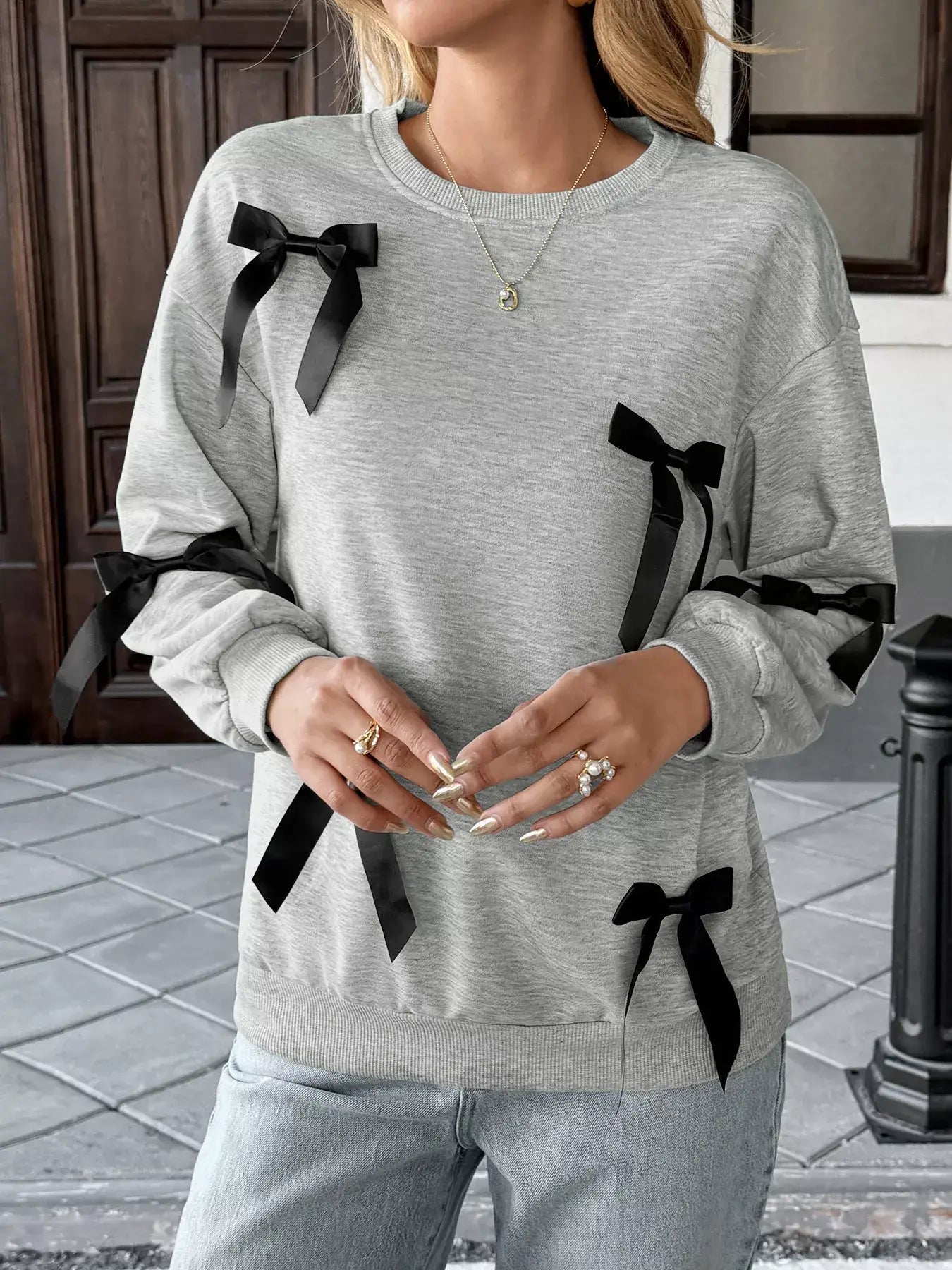 Model wearing a Bow Detail Round Neck Sweatshirt with stylish bow accents on sleeves in a casual setting.