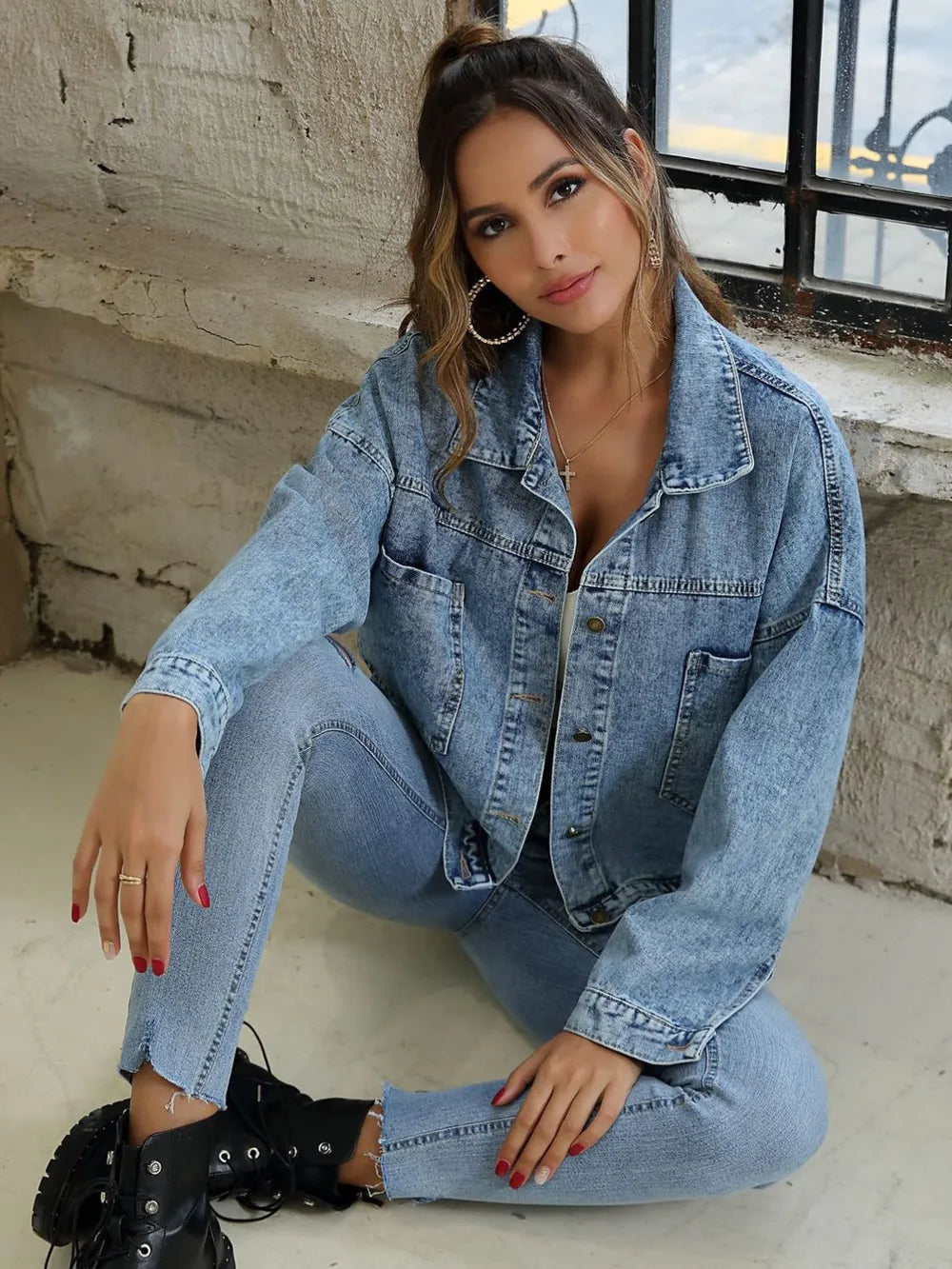 Woman wearing a Button Down Drop Shoulder Denim Jacket, sitting casually in light blue jeans.