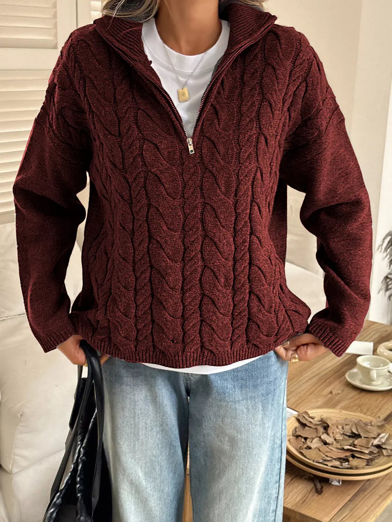 Woman wearing a zip collar cable-knit sweater in burgundy, showcasing its chunky knit texture and zip-up collar.