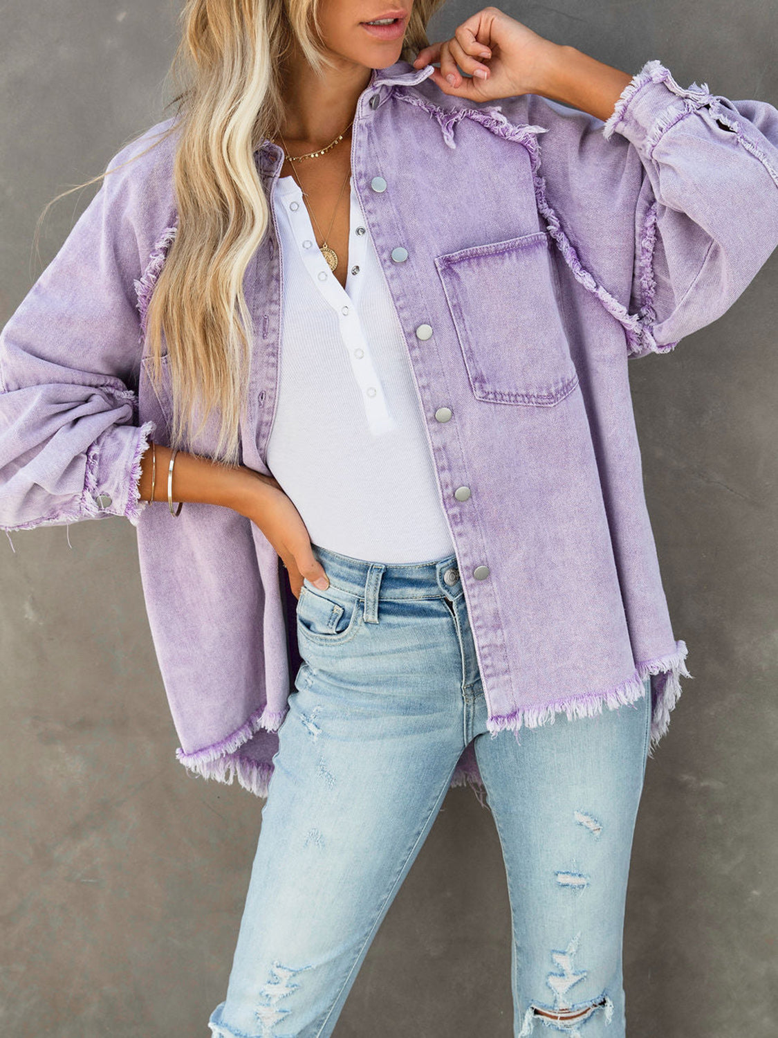Model wearing a Button Down Raw Hem Denim Jacket, purple color, styled with a white henley and distressed jeans.