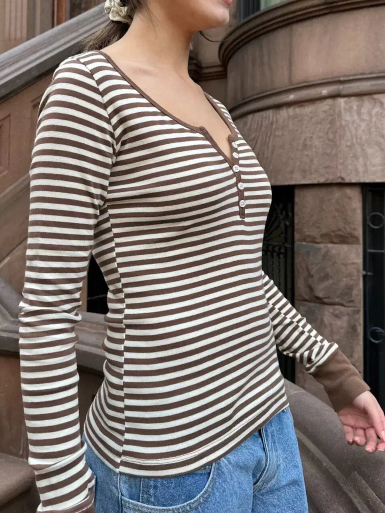 Side view of a woman wearing a stylish striped long sleeve henley t-shirt during casual outdoor wear.