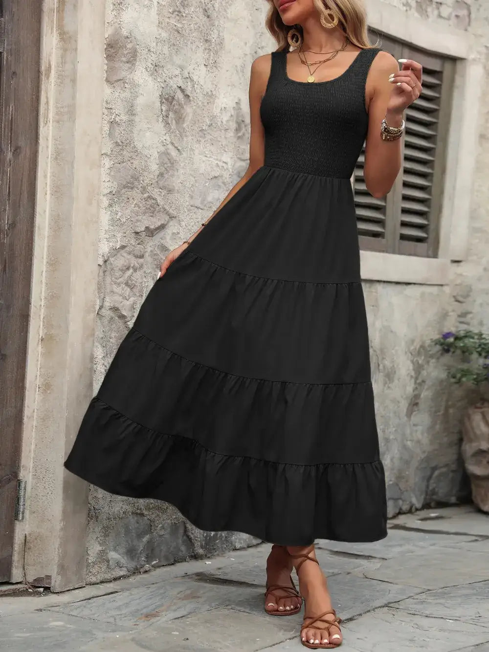 Ivy Lane black smocked scoop neck sleeveless tank dress with tiered ruffle skirt on a stone background.