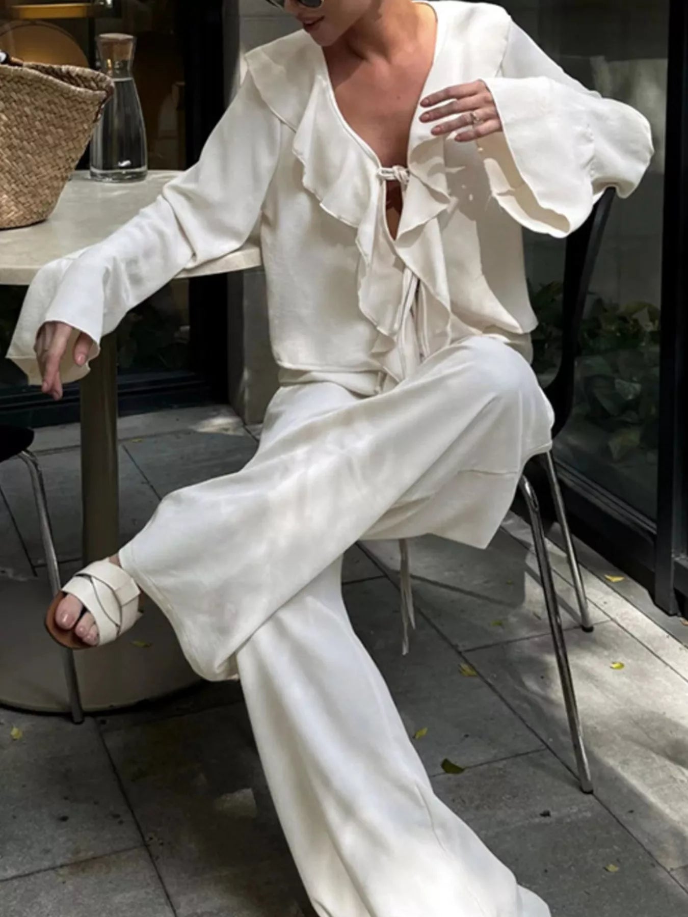 Woman wearing Ruffle Trim Tie Front Top and Pants Set, sitting outdoors in a stylish and relaxed pose.