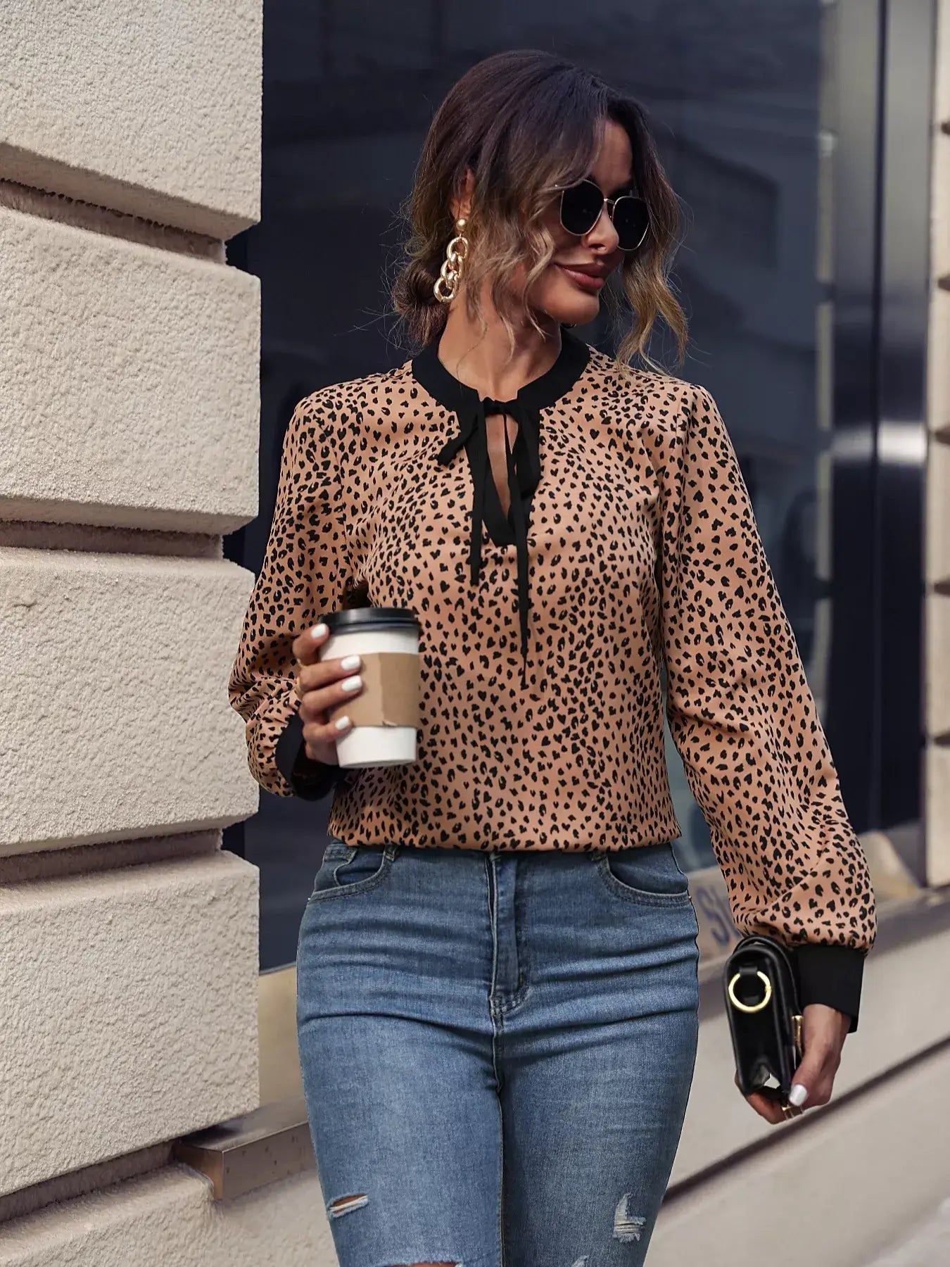 Woman wearing an animal print contrast trim tie front blouse with coffee in hand and stylish sunglasses.