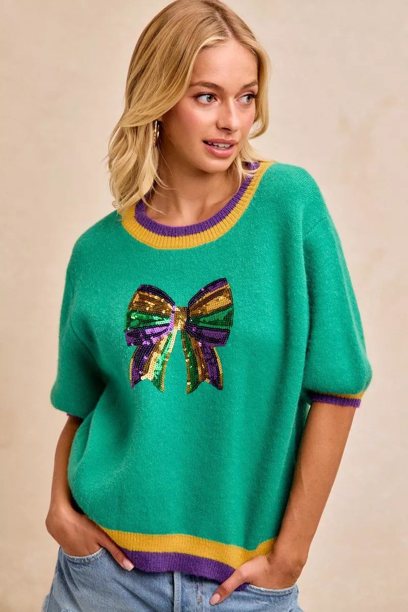 BiBi Mardi Gras Sequin Ribbon Patched Sweater featuring a colorful sequin bow design on a vibrant green sweater.
