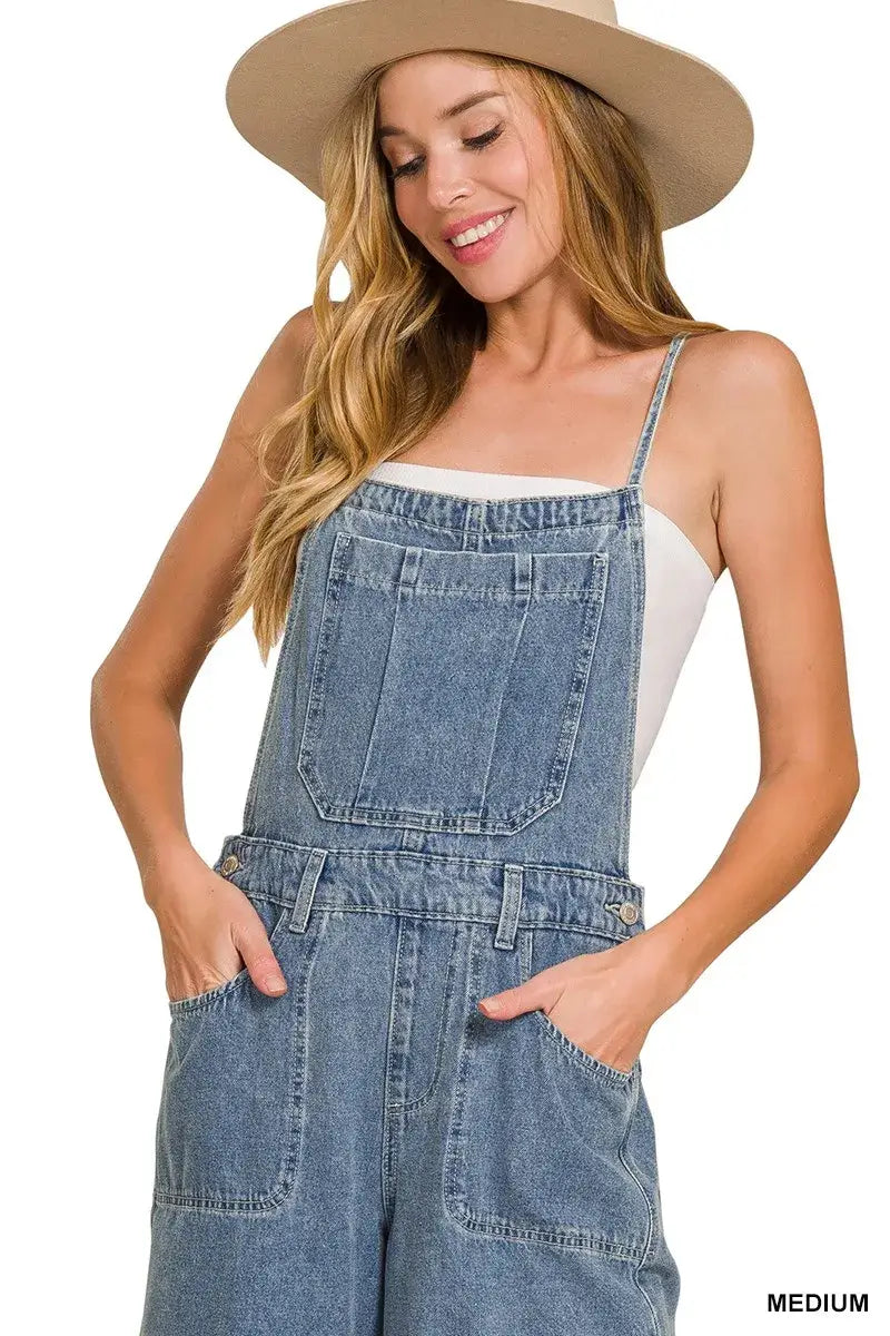 Woman wearing Zenana Denim Wide Leg Overalls in medium wash with pockets and a hat, showcasing casual style.