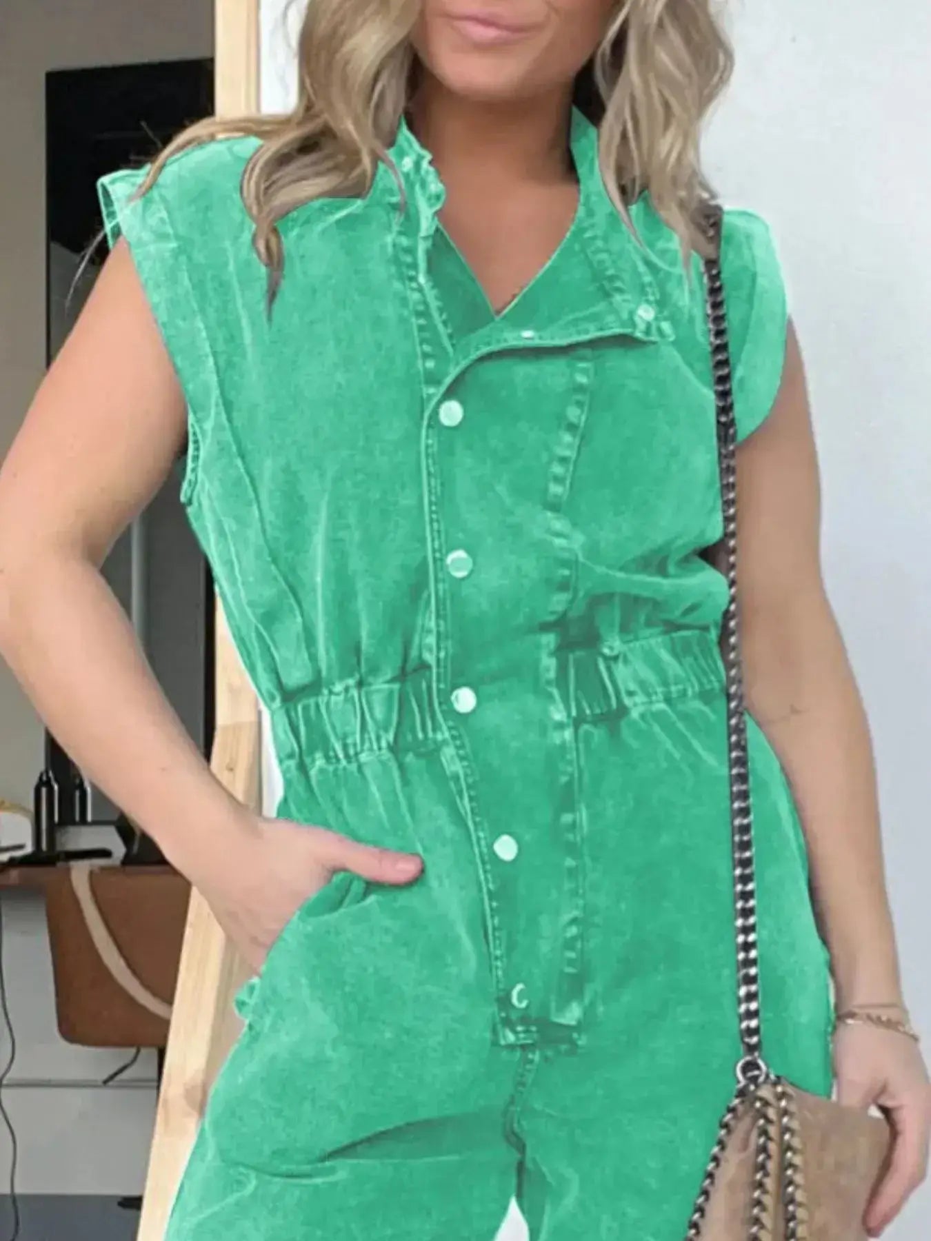 Plus size woman wearing a green cap sleeve denim jumpsuit with button front and belted waist.