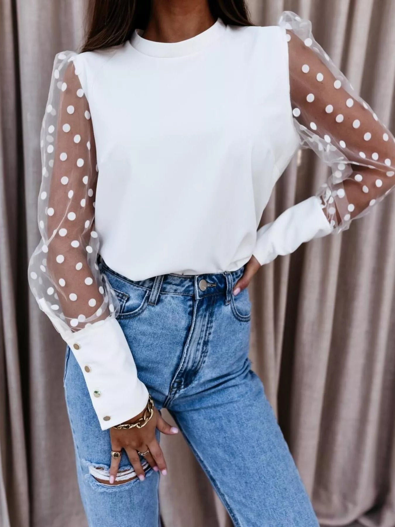 Model wearing a Polka Dot Mesh Sleeve Blouse, featuring sheer sleeves and a stylish design paired with jeans.