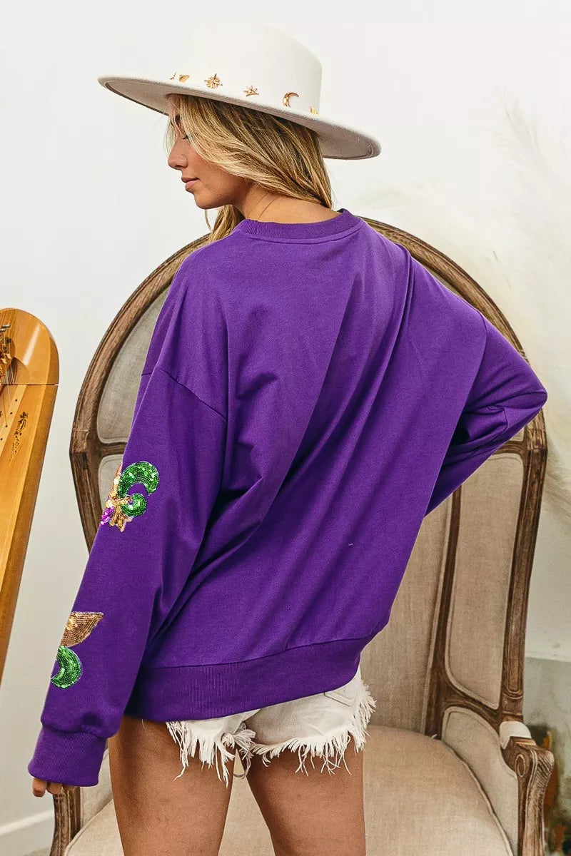 BiBi Fleur De Lis Sequin Patches Mardi Gras Sweatshirt in purple with sequin patches and a stylish hat.
