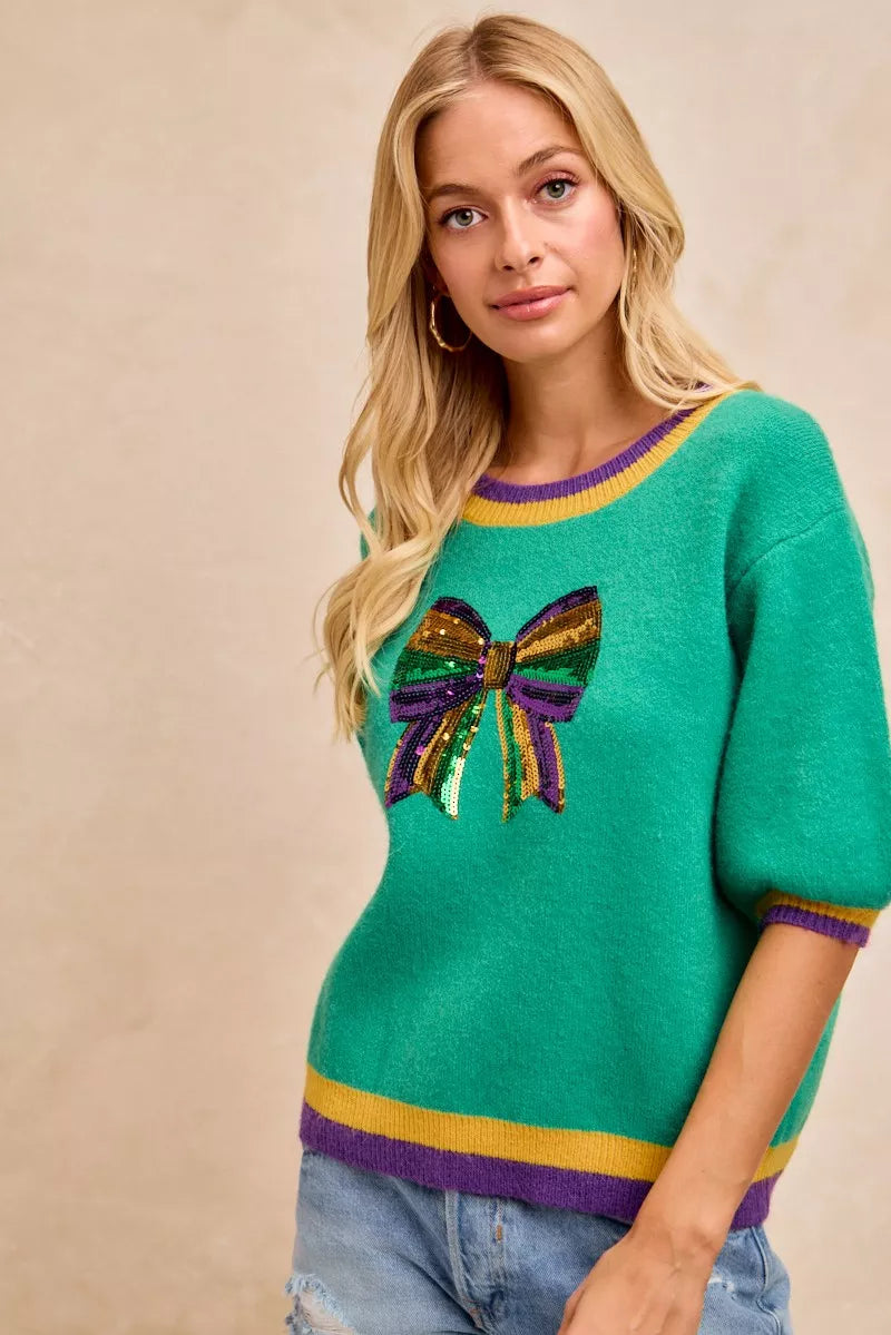 BiBi Mardi Gras Sequin Ribbon Patched Sweater showcasing vibrant green color and colorful sequin bow design.