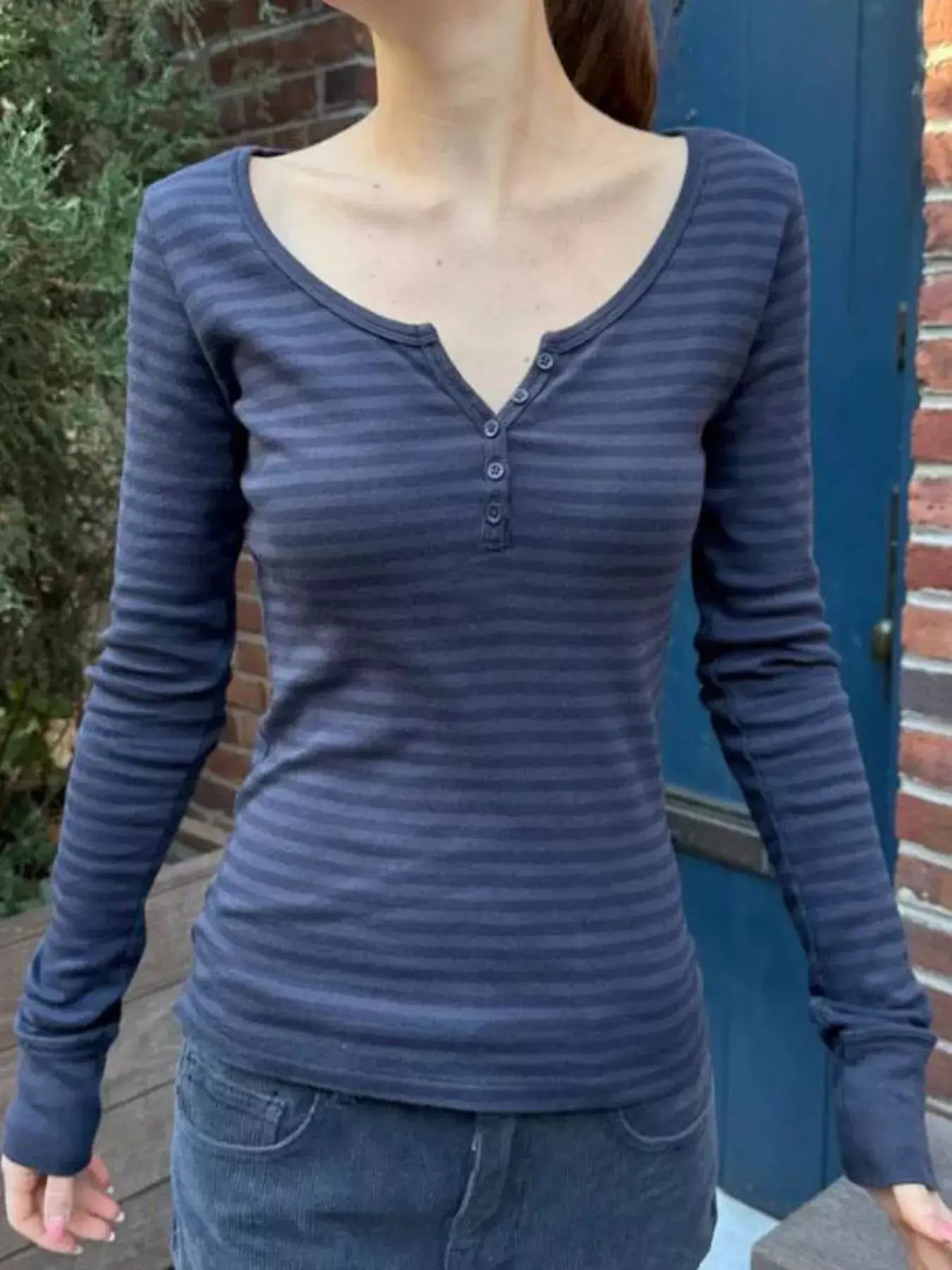 Model wearing a striped long sleeve Henley t-shirt with buttoned design, suitable for casual wear.