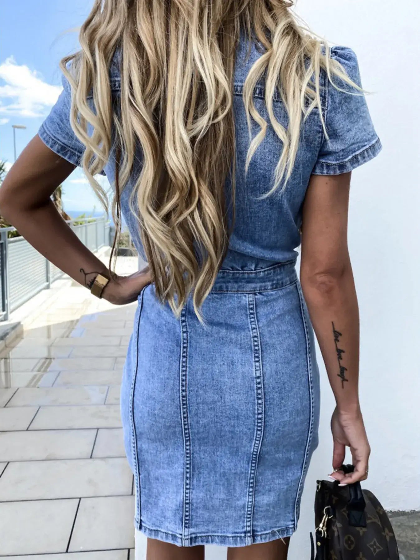 Back view of a woman wearing a casual button front short sleeve denim dress with long hair, ideal for summer outings.