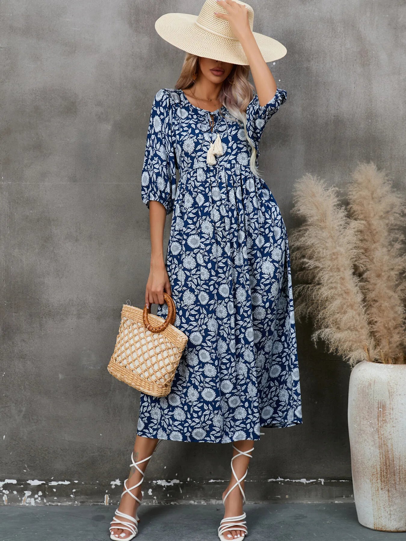 Model wearing a Printed Tie Neck Midi Dress in navy floral pattern, accessorized with a straw hat and bag.
