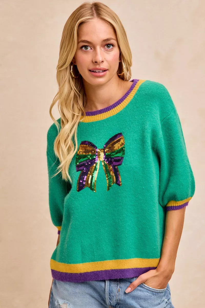 BiBi Mardi Gras Sequin Ribbon Patched Sweater featuring a sequin bow and vibrant colors, perfect for festive style.