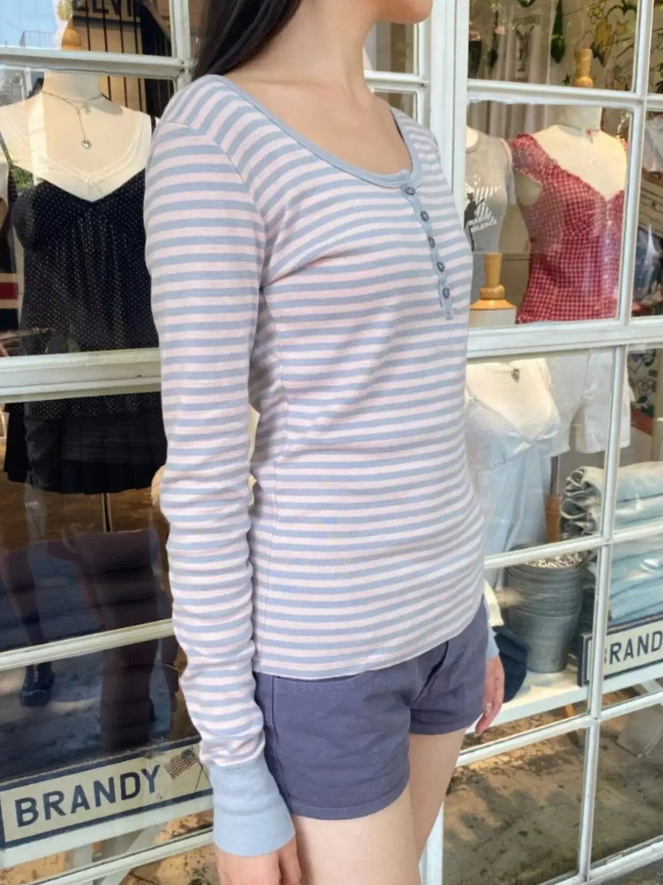 Model wearing a striped long sleeve Henley T-shirt with buttons, showcasing a casual style.