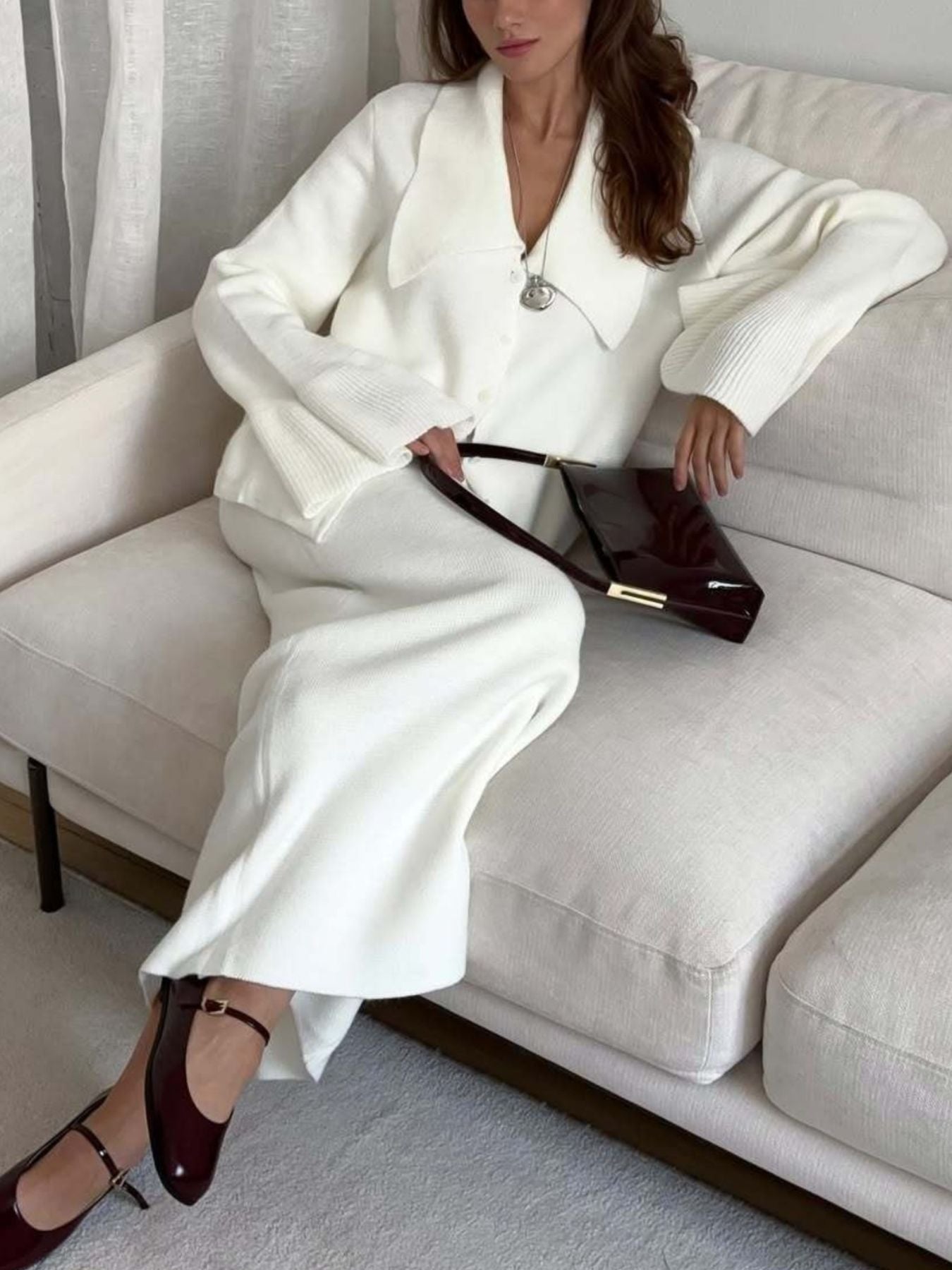 Woman wearing a Button Down Cardigan and Skirt Knit Set while sitting on a couch, holding a handbag.