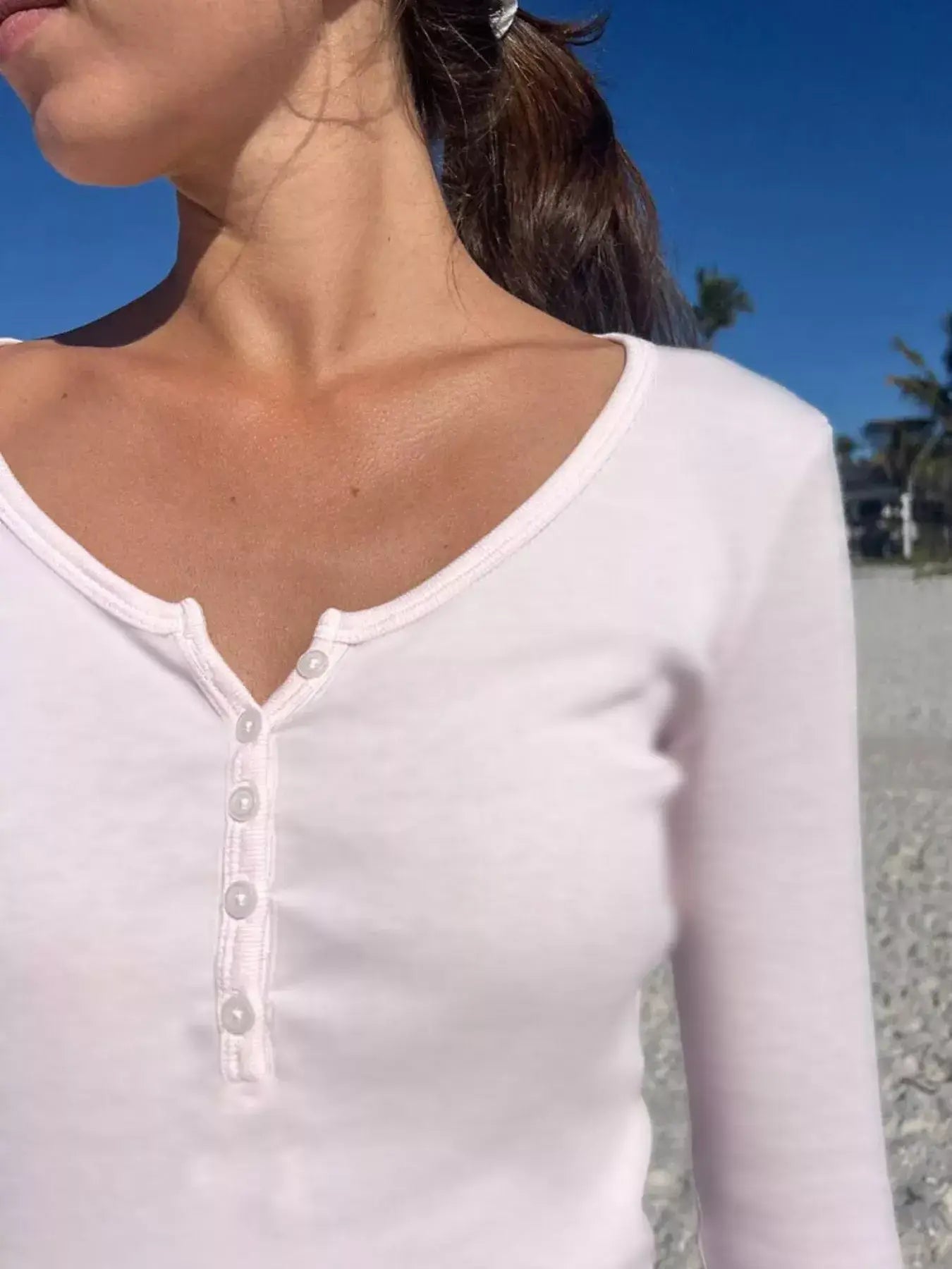 Close-up of a woman wearing a light pink striped long sleeve Henley T-shirt with buttoned design on the beach.