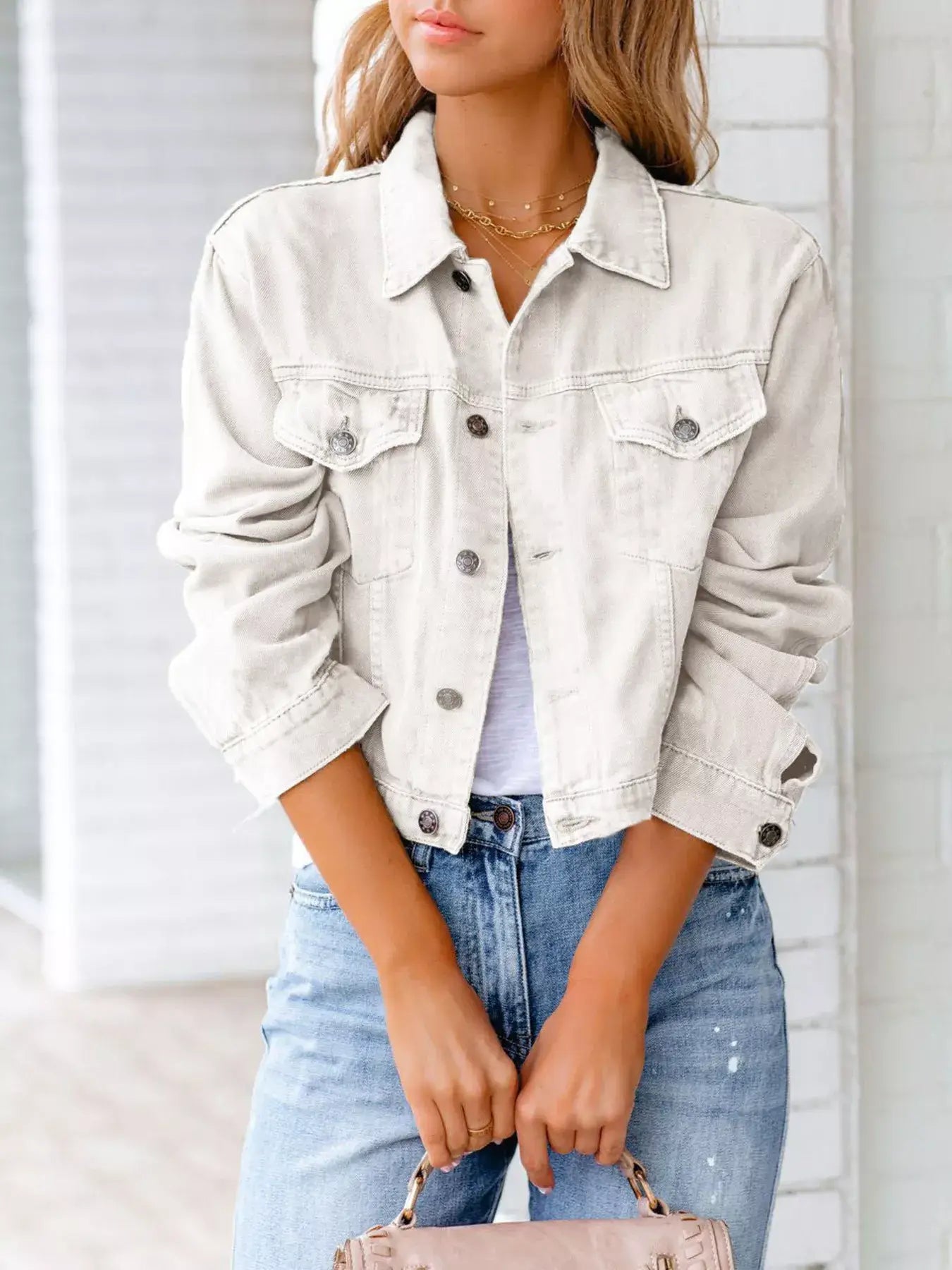 Model wearing a white button-up long sleeve denim jacket with distressed jeans, showcasing a stylish casual look.