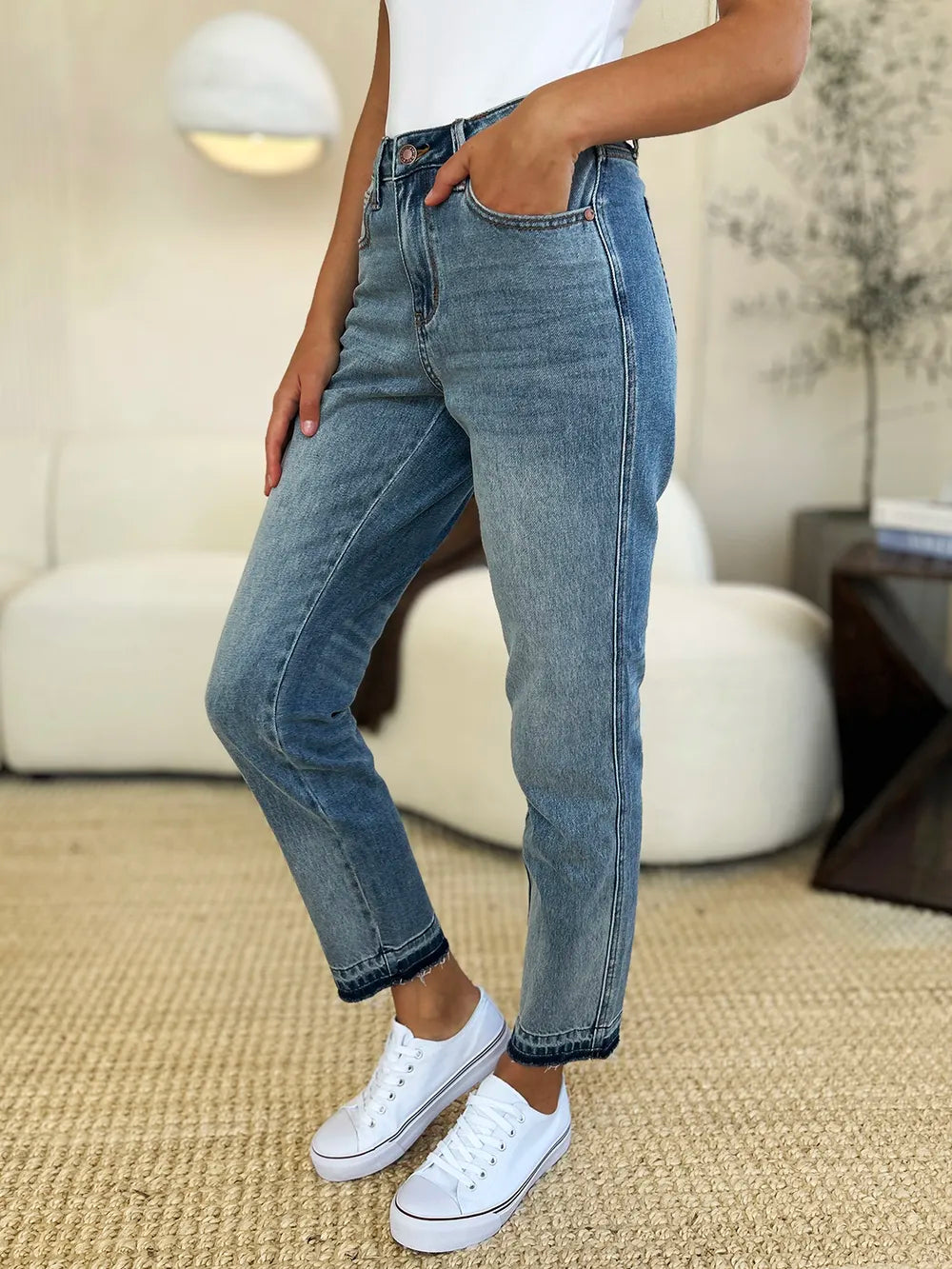 Model wearing Mid Rise Magic Release Hem Jeans with white sneakers in a stylish living room setting.