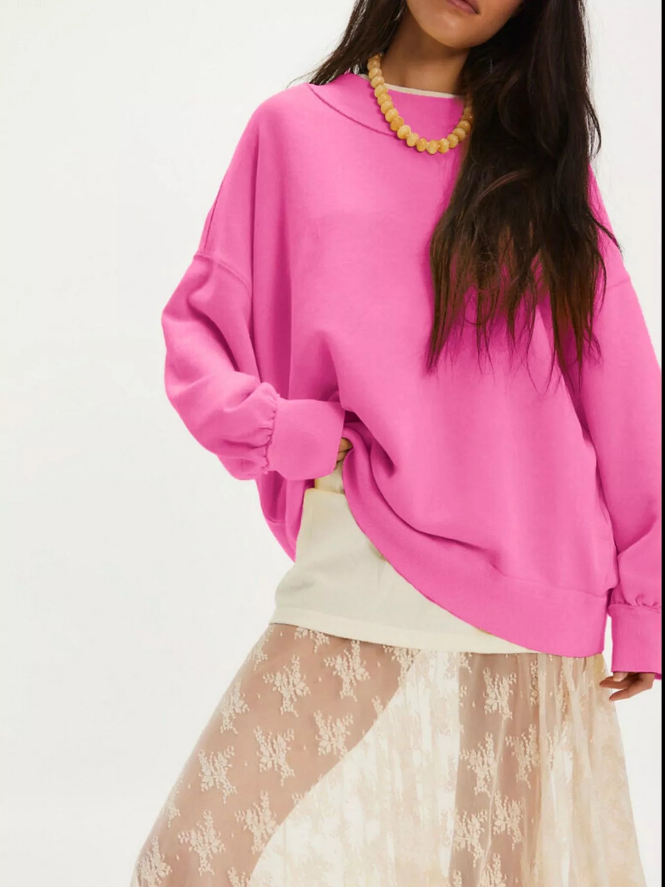 Woman wearing an Exposed Seam Dropped Shoulder Sweatshirt in pink, styled with a layered skirt and accessorized with a necklace.
