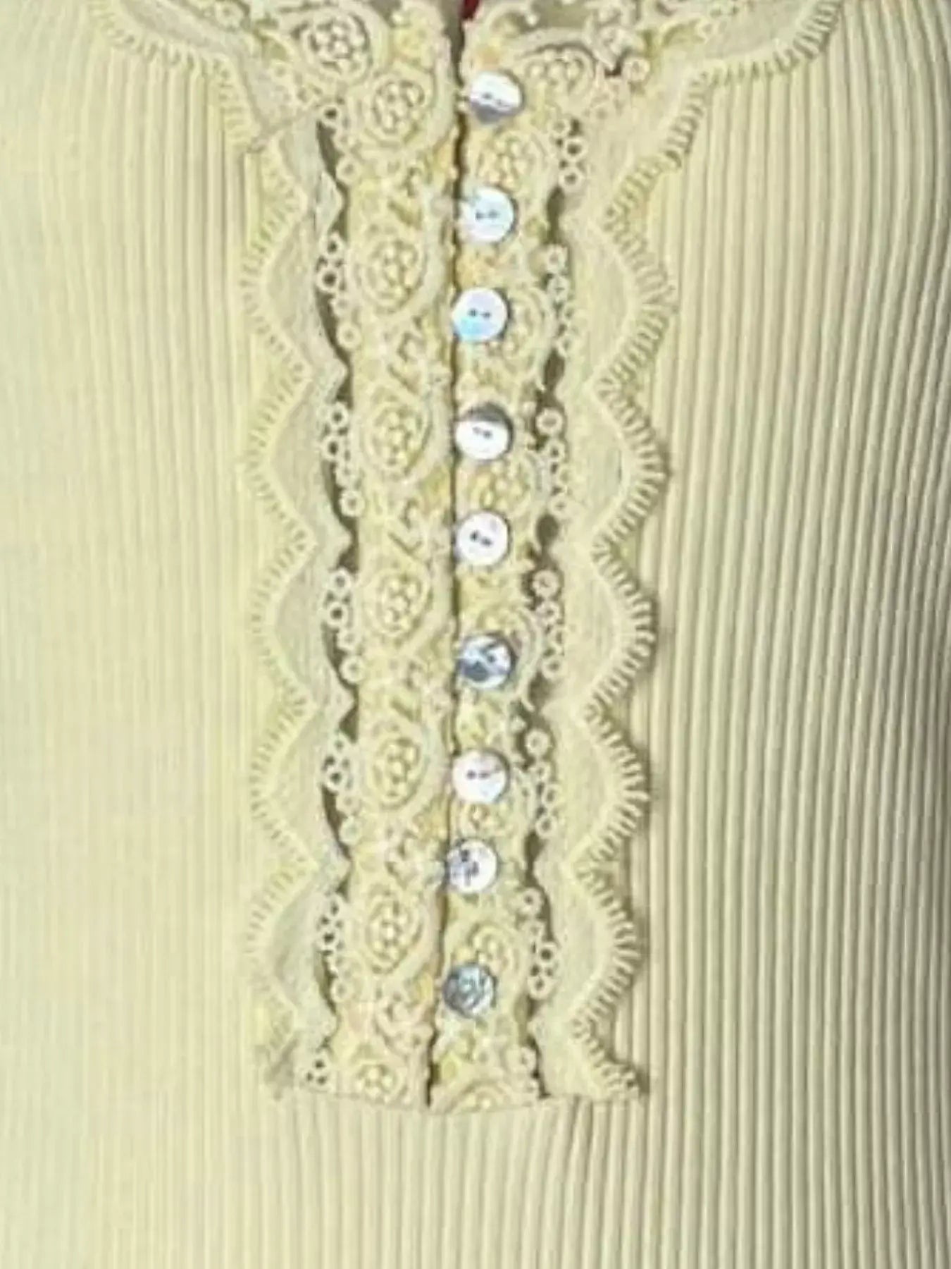 Close-up of lace trim and button details on a ribbed long sleeve t-shirt in light yellow.