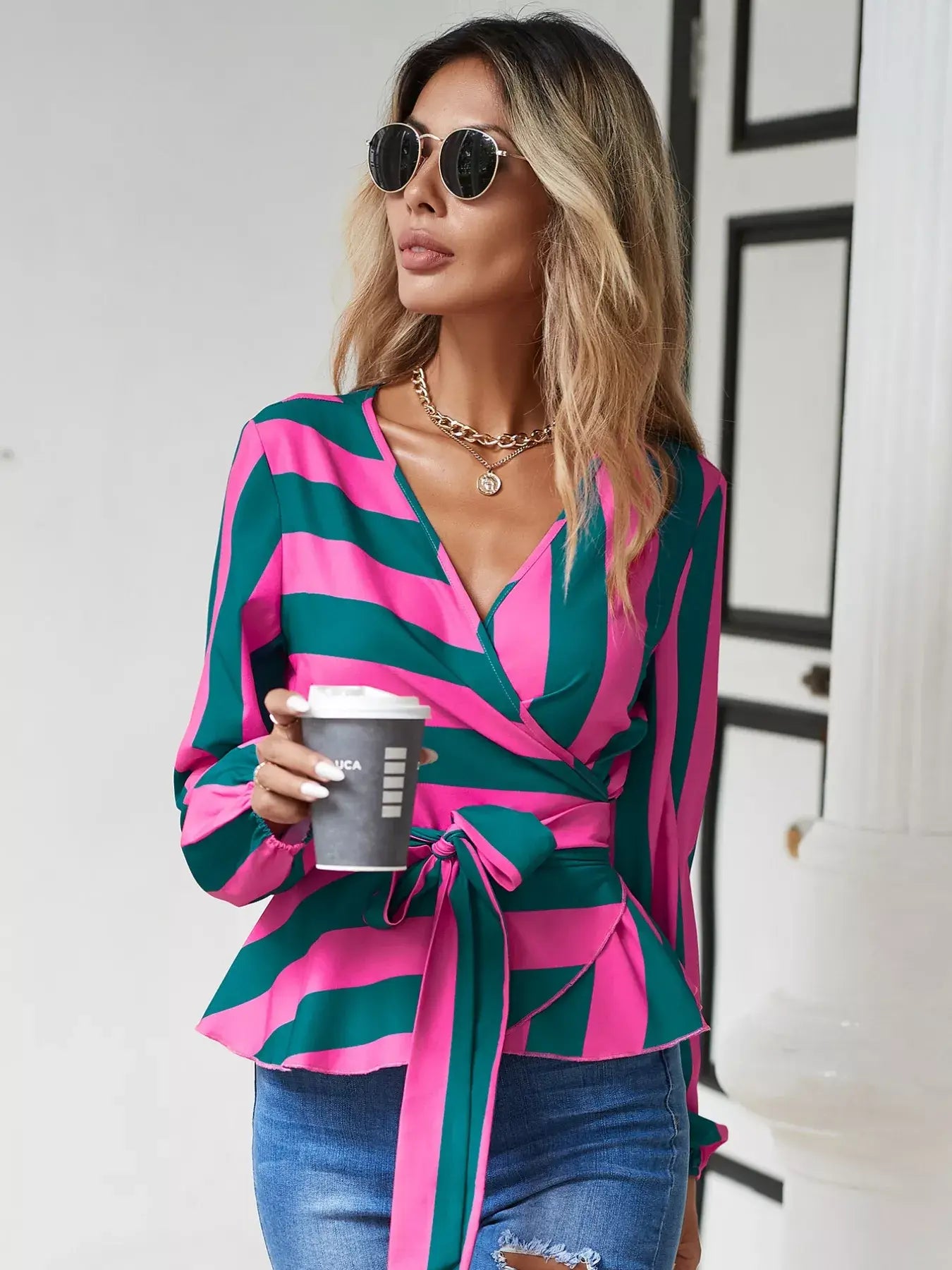 Woman wearing a striped wrap blouse with tie detail, sipping coffee in a chic outdoor setting.