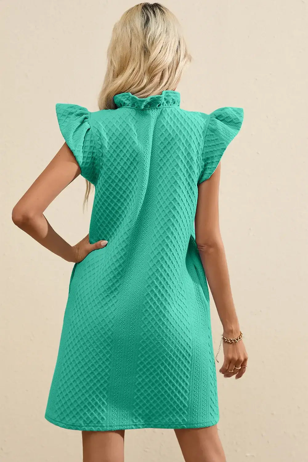 Back view of a teal ruffled V-neck cap sleeve mini dress with a textured pattern.