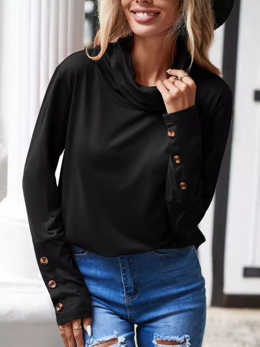 Woman smiling in a cowl neck long sleeve blouse, featuring stylish button details, paired with denim shorts.